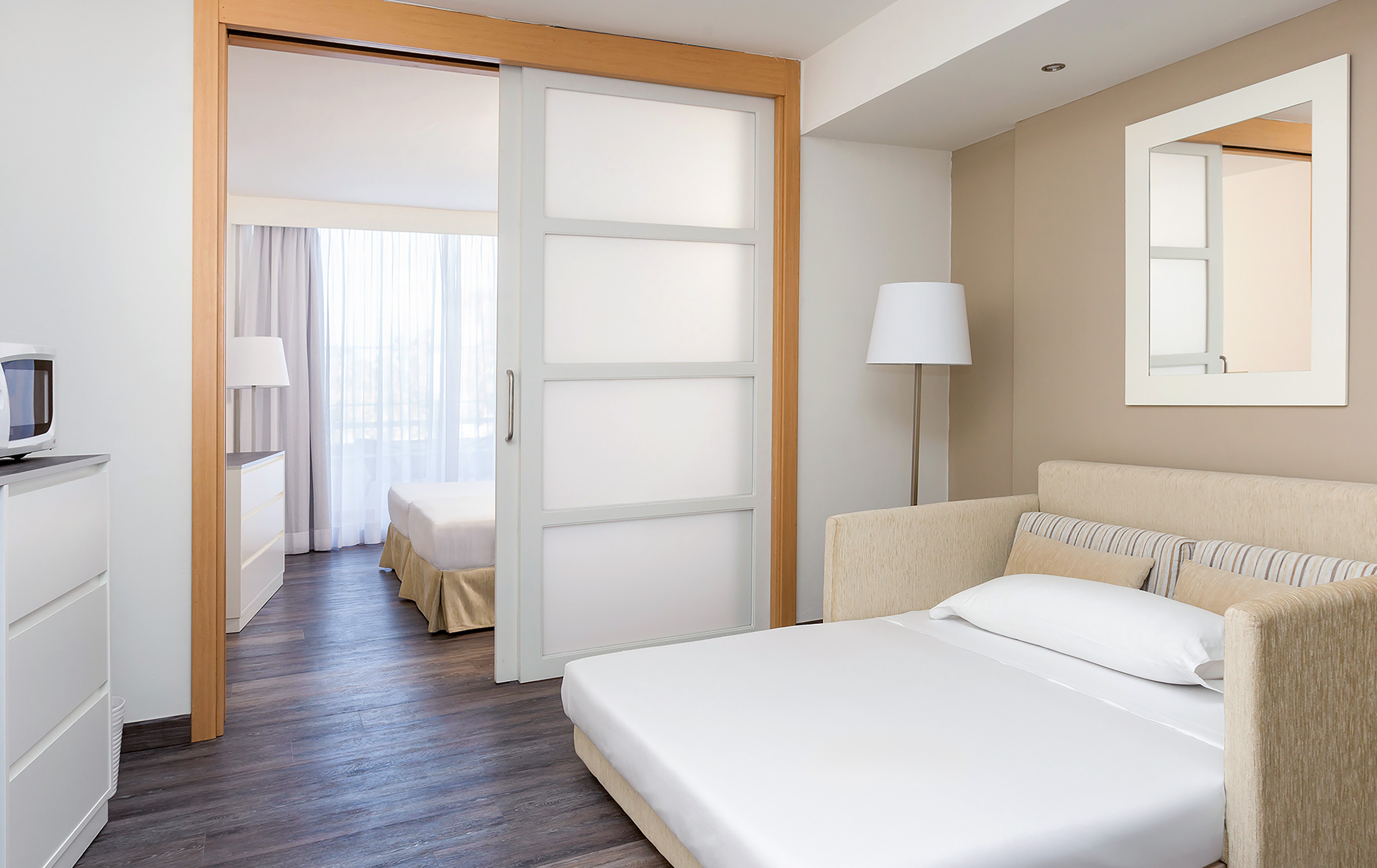 Modern hotel suite with sofa bed and separate bedroom behind sliding door.
