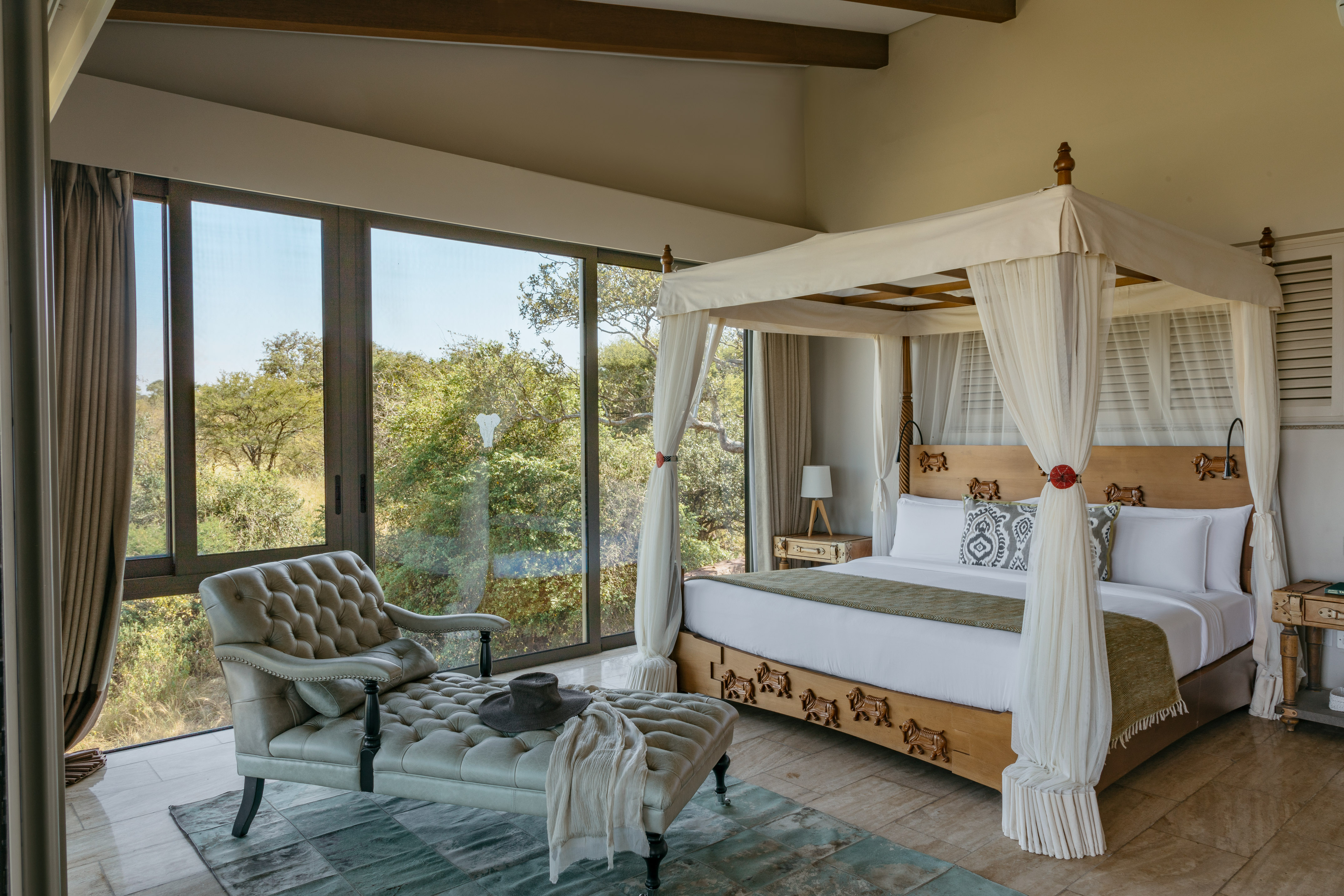 Luxury safari bedroom with four-poster bed, large windows, and savanna view.