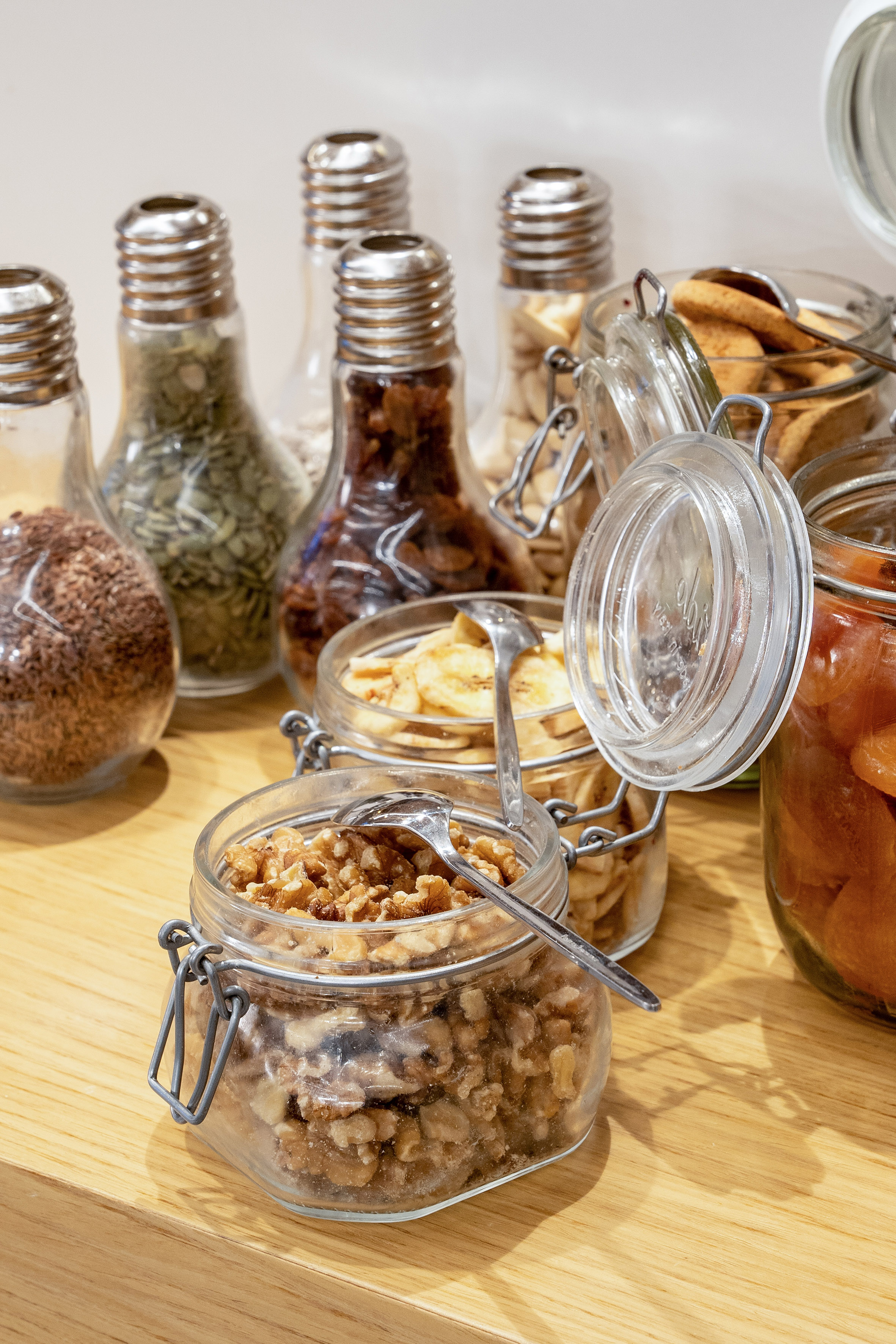 Variety of nuts, seeds, and dried fruit in clear glass jars on wooden countertop.