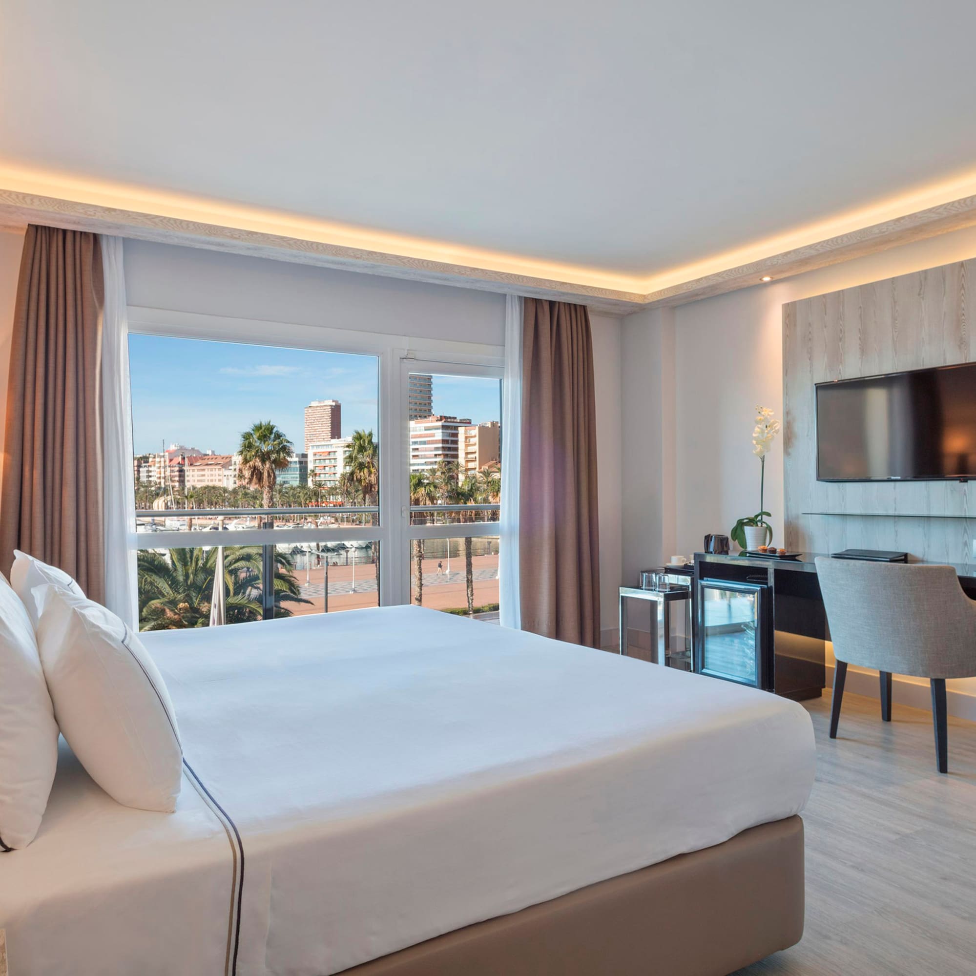 Hotel room with king bed, waterfront city view, modern desk, and TV.