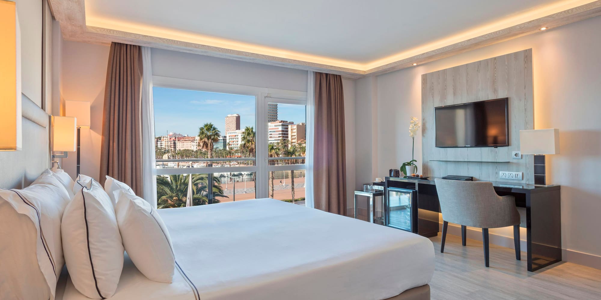 Hotel room with king bed, waterfront city view, modern desk, and TV.