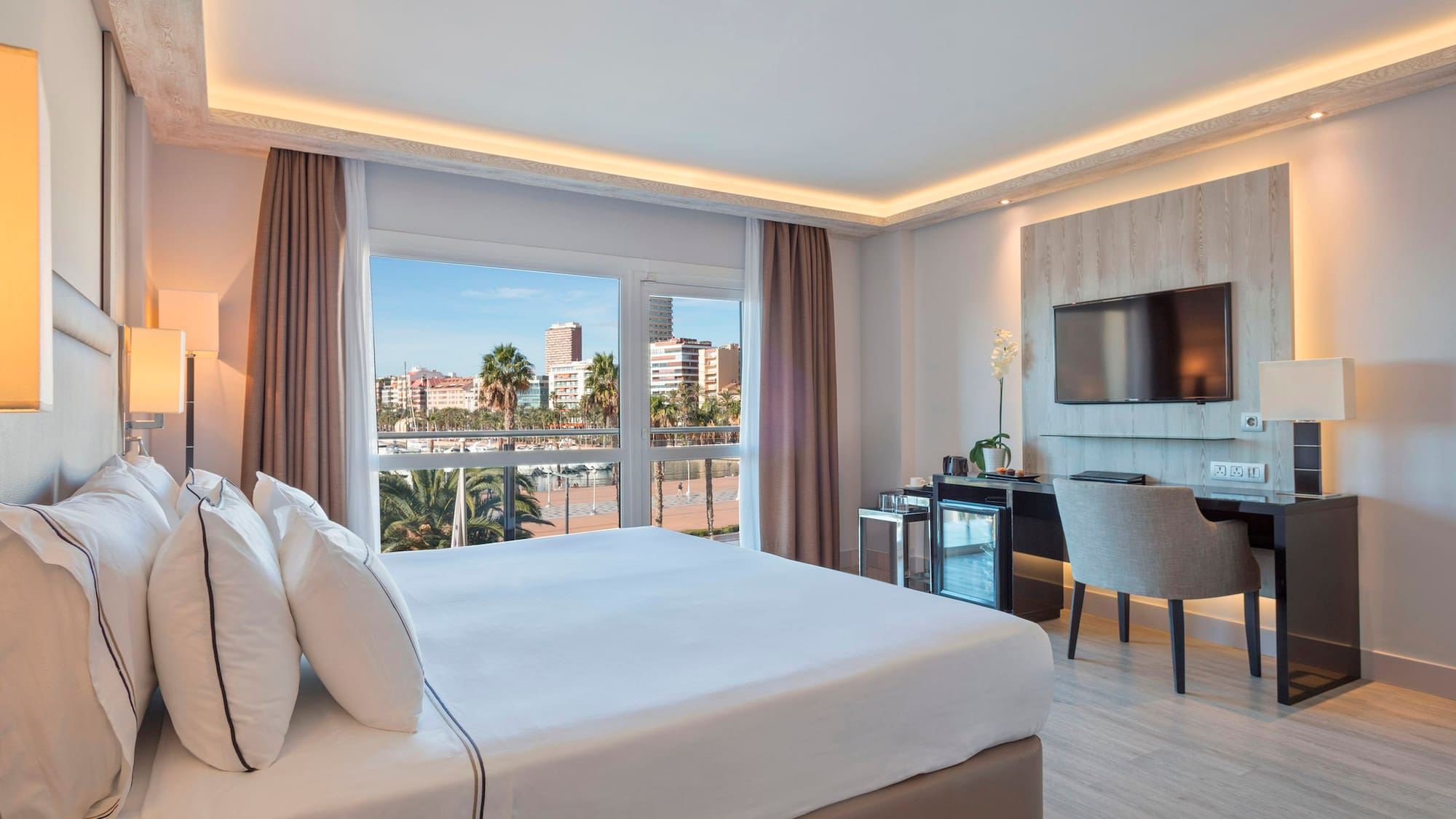 Hotel room with king bed, waterfront city view, modern desk, and TV.