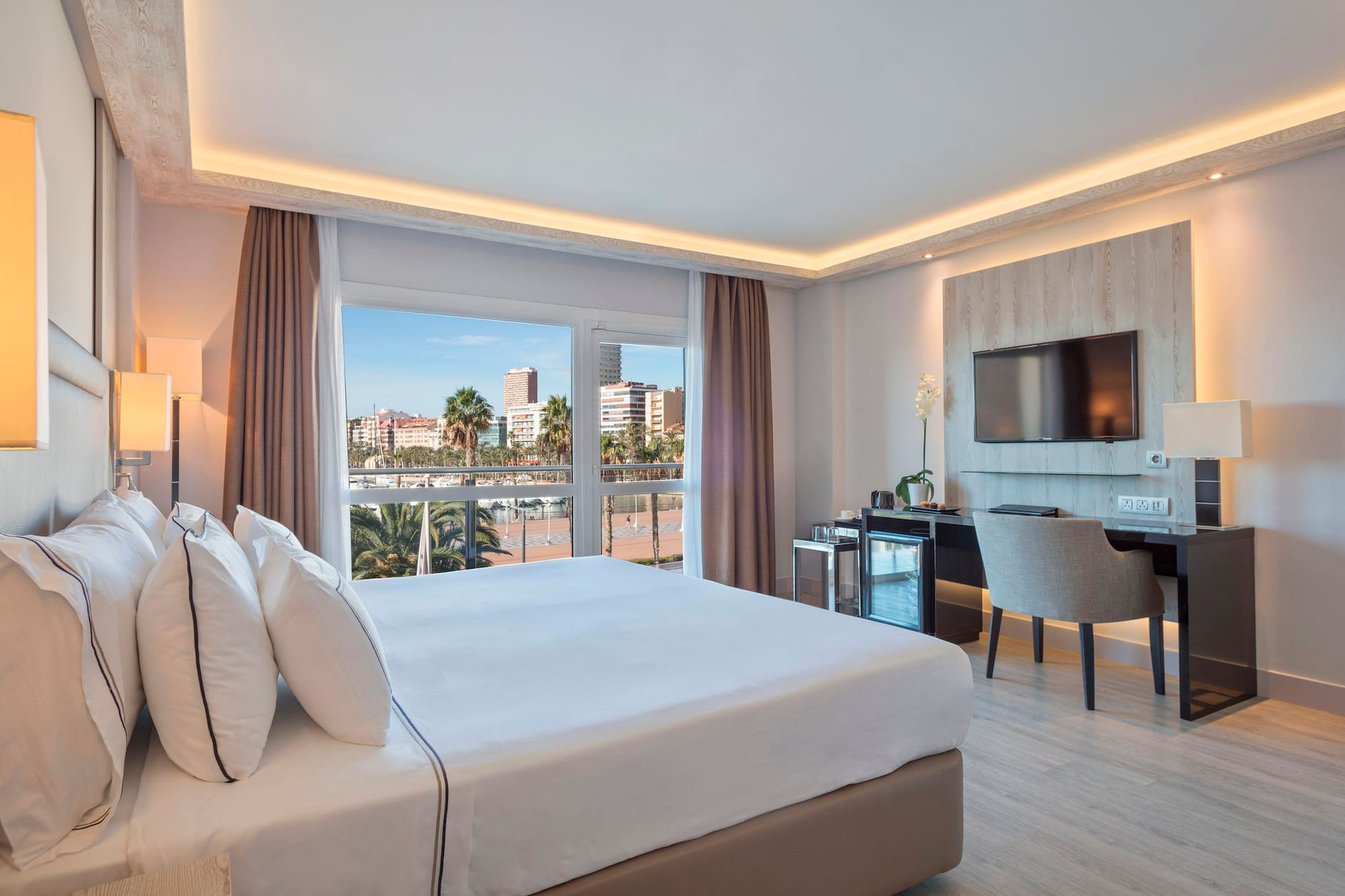 Hotel room with king bed, waterfront city view, modern desk, and TV.