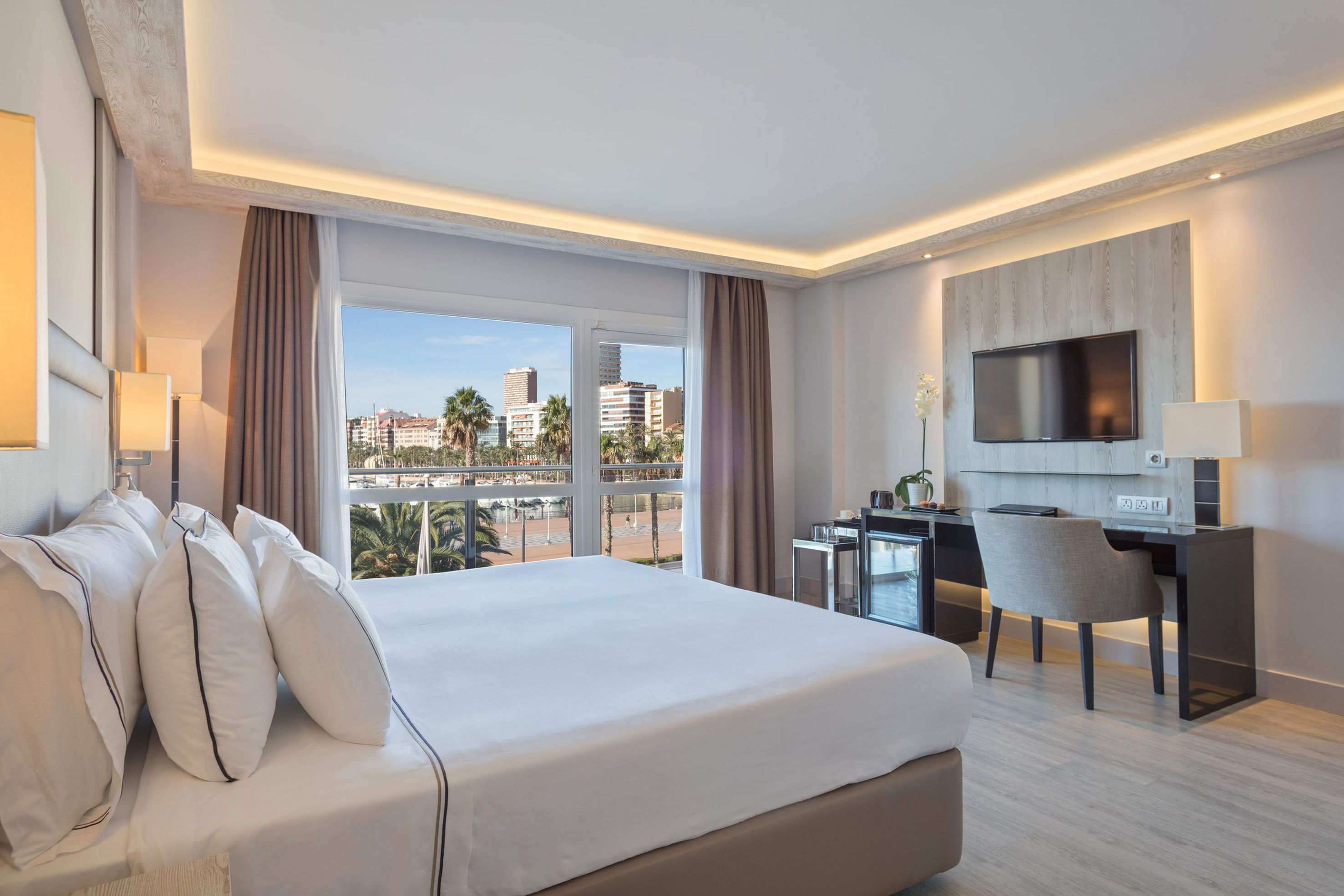 Hotel room with king bed, waterfront city view, modern desk, and TV.