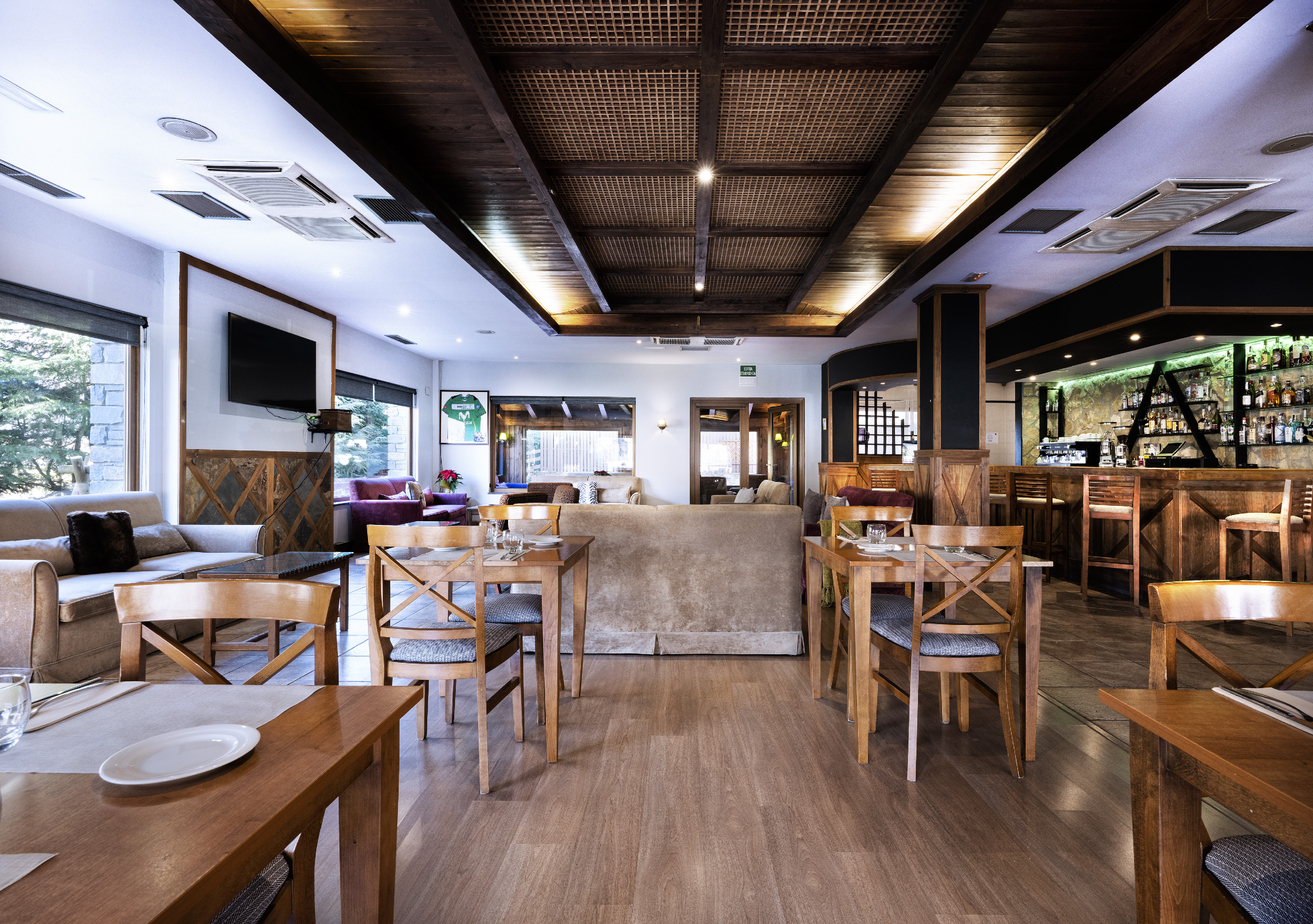 Warm restaurant and bar interior with wooden tables, lounge seating, and a lit bar.