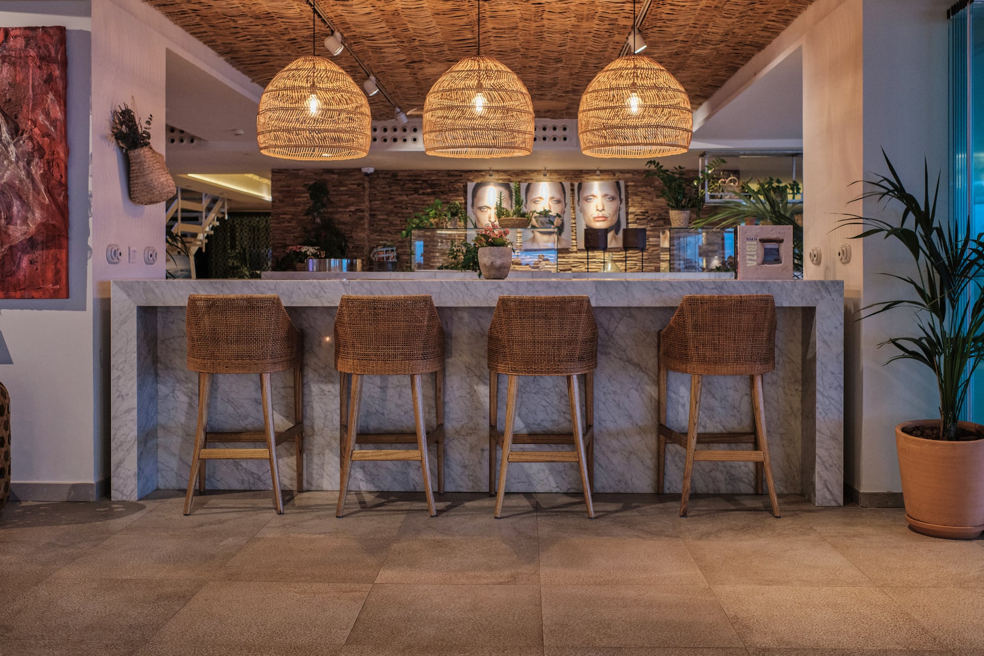 Marble bar with rattan stools and woven pendant lights in a modern hotel lounge.