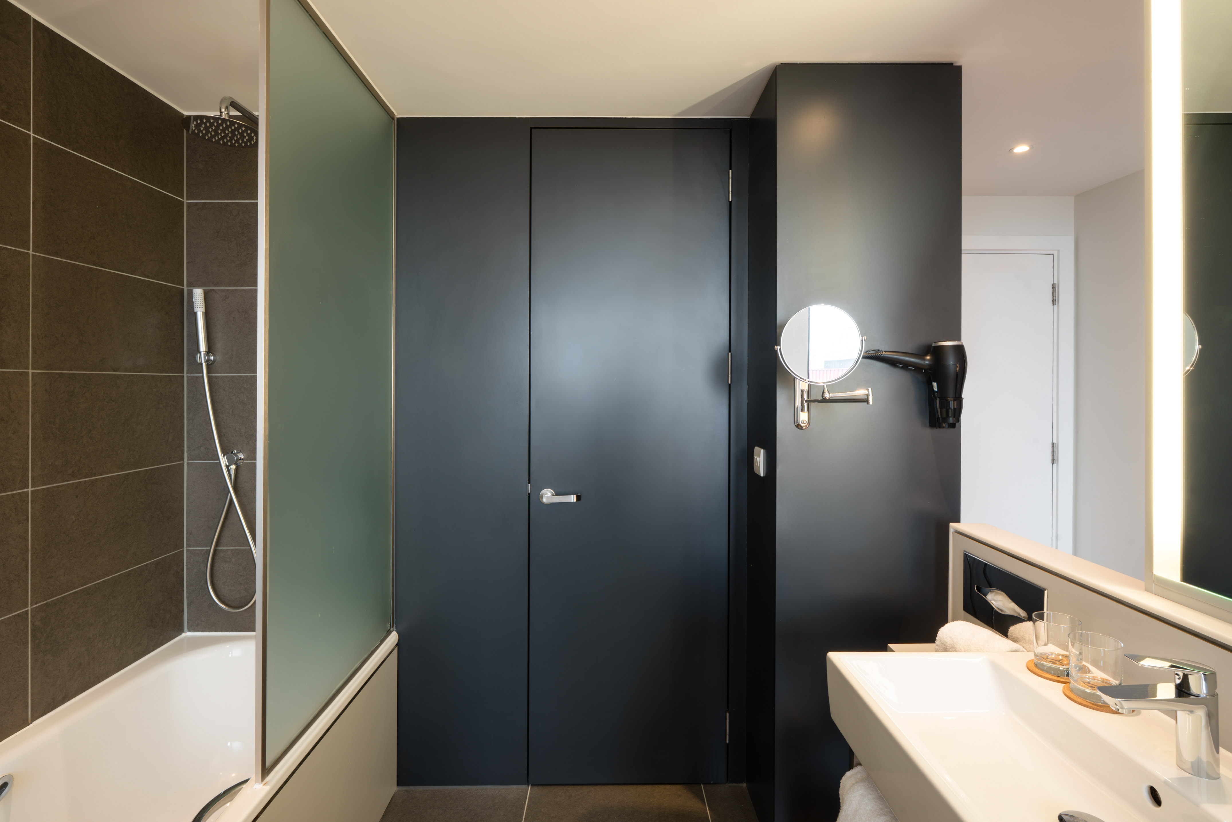 Modern hotel bathroom with shower-tub, dark gray walls, white vanity, and mirror.