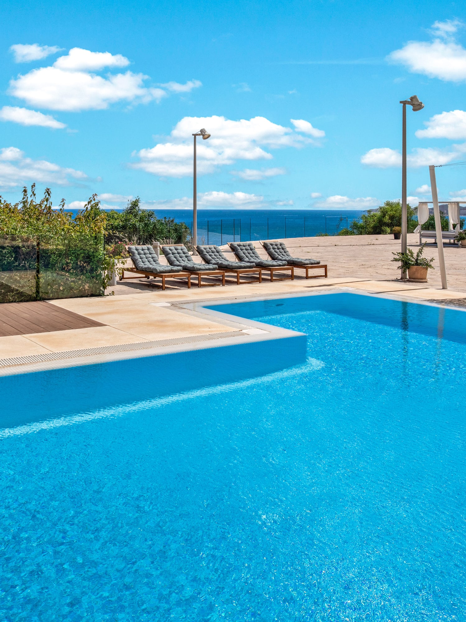 Resort swimming pool with ocean view, sunbeds, and blue sky.