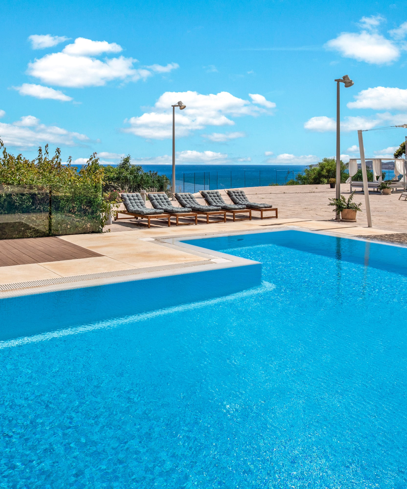 Resort swimming pool overlooking the ocean with sun loungers and blue sky.