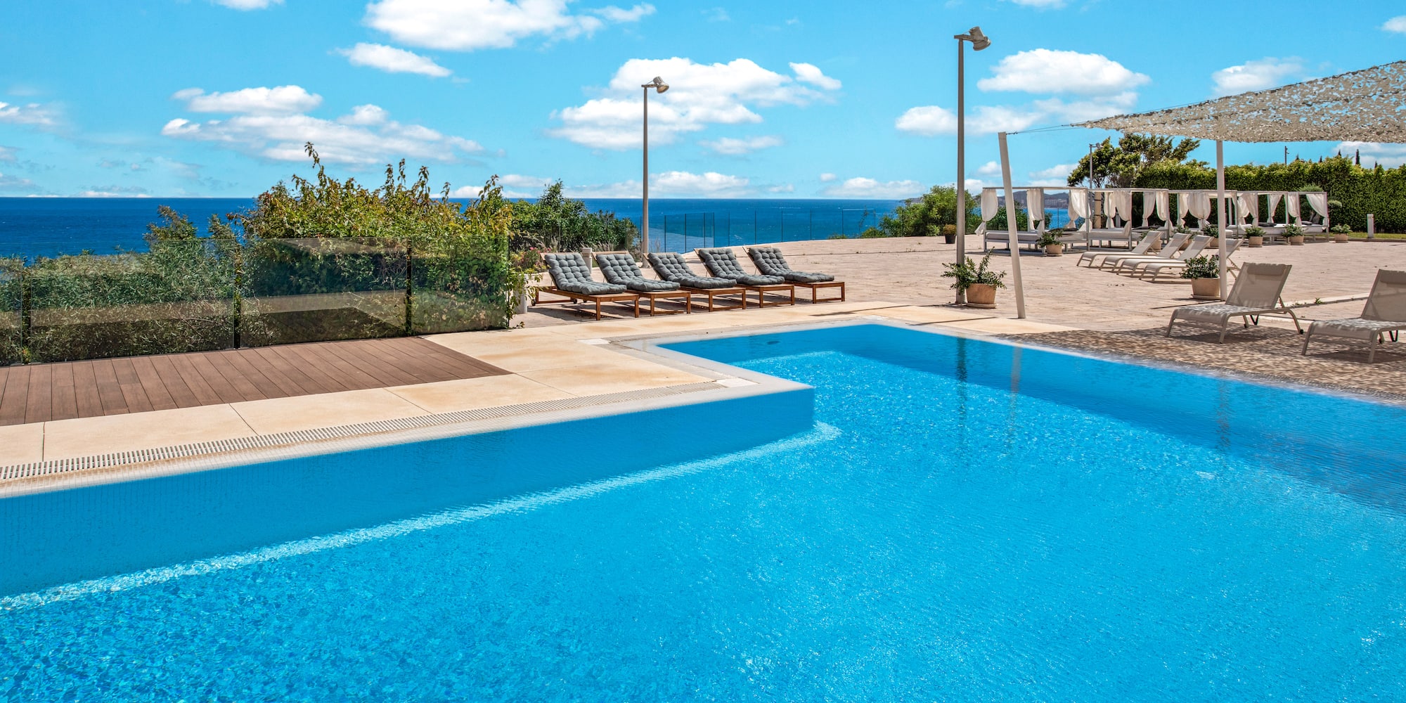 Resort swimming pool with ocean view, sunbeds, and blue sky.