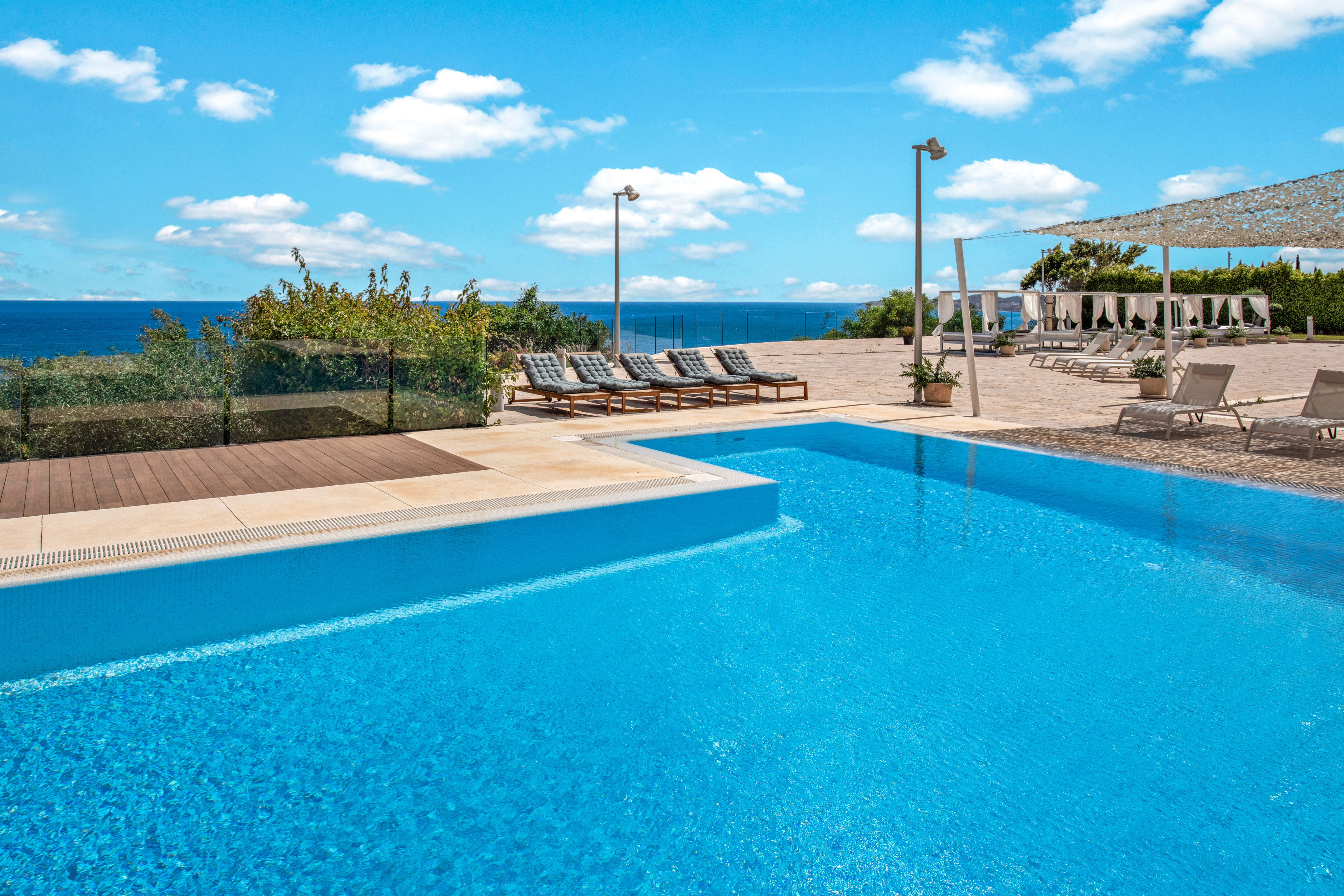 Resort swimming pool with ocean view, sunbeds, and blue sky.