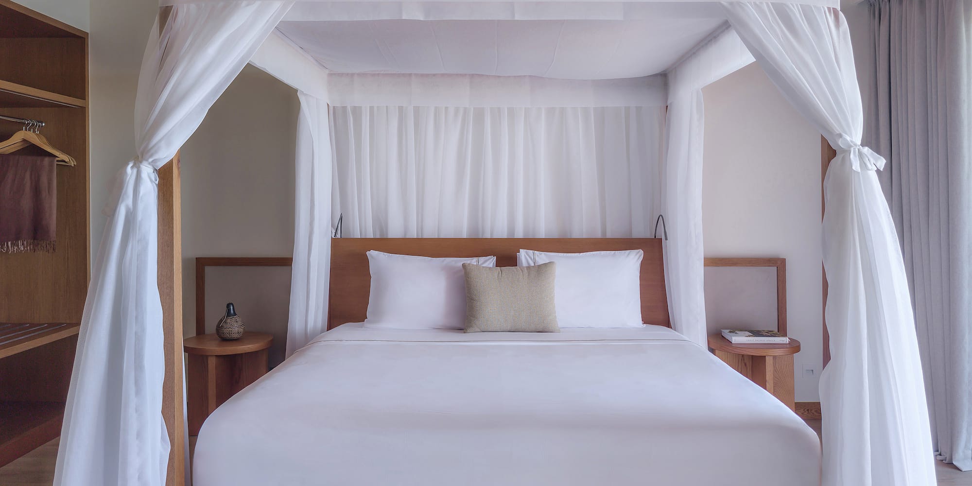 Luxury four-poster canopy bed with white drapes in a modern tropical bedroom.