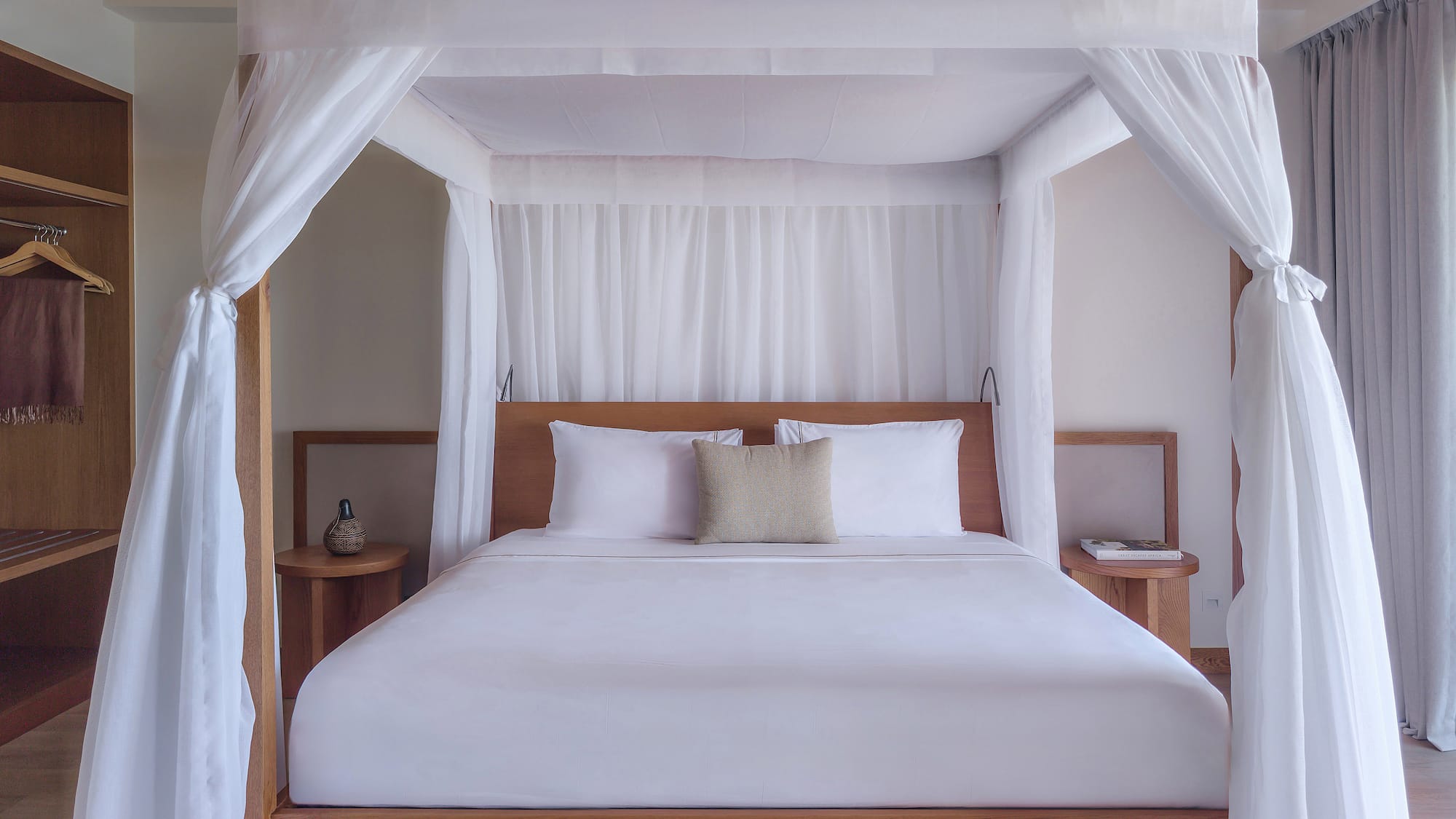 Luxury four-poster canopy bed with white drapes in a modern tropical bedroom.