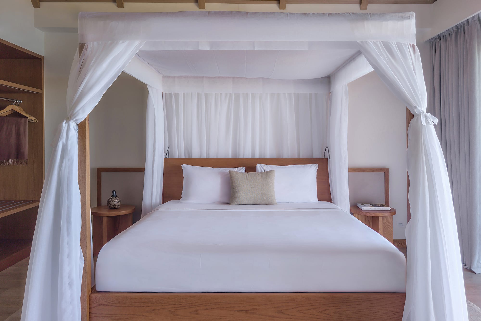 Luxury four-poster canopy bed with white drapes in a modern tropical bedroom.