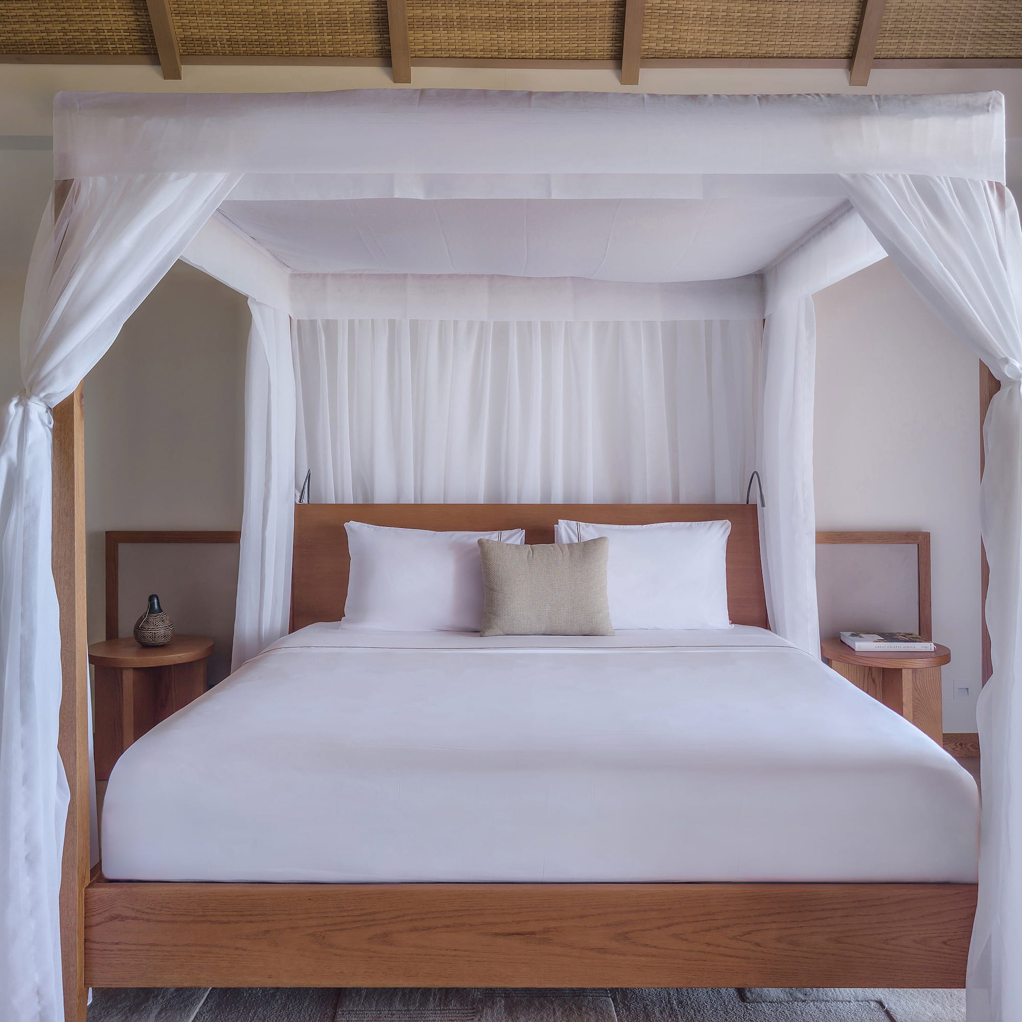Luxury four-poster canopy bed with white drapes in a modern tropical bedroom.