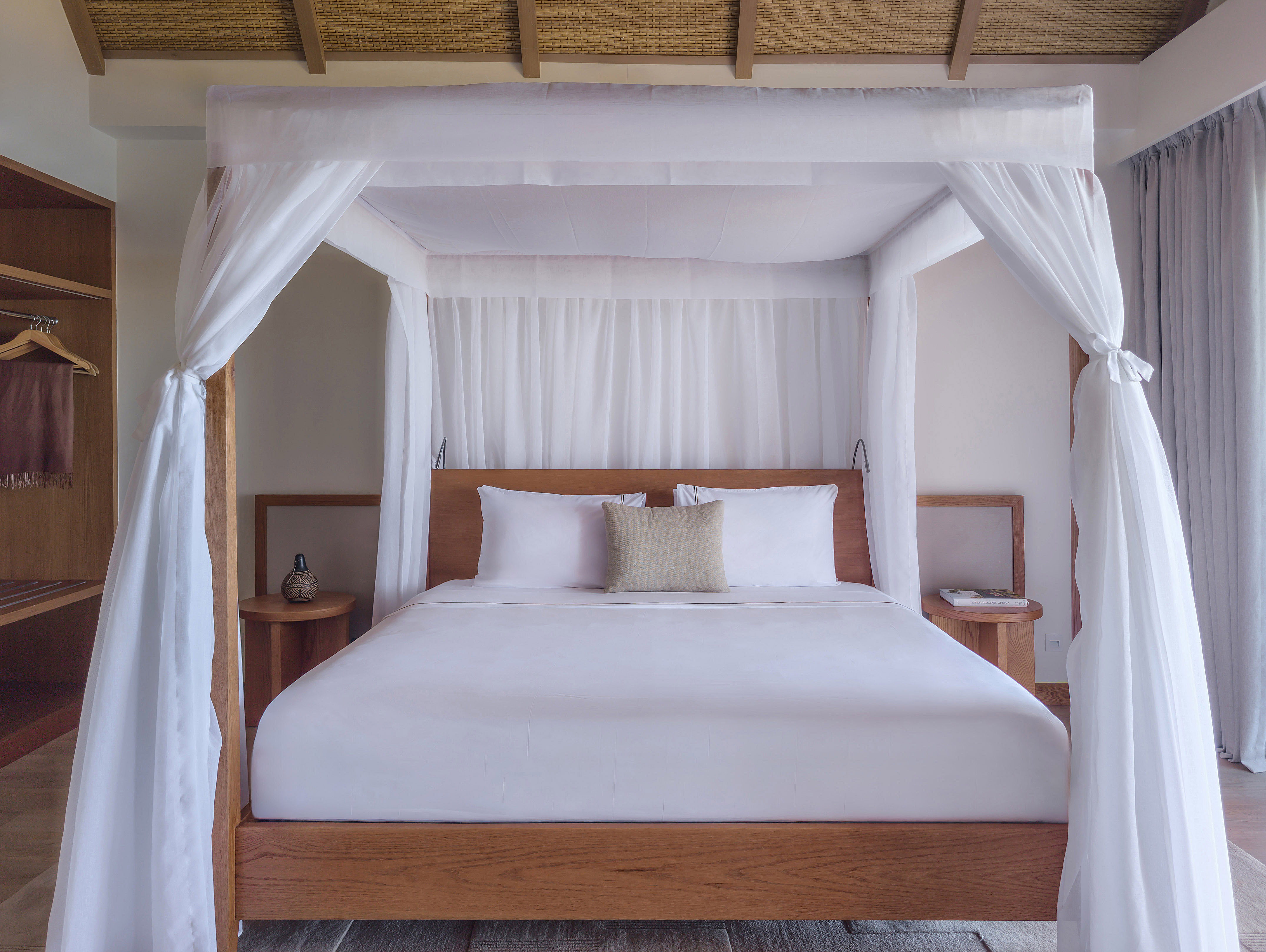 Luxury four-poster canopy bed with white drapes in a modern tropical bedroom.