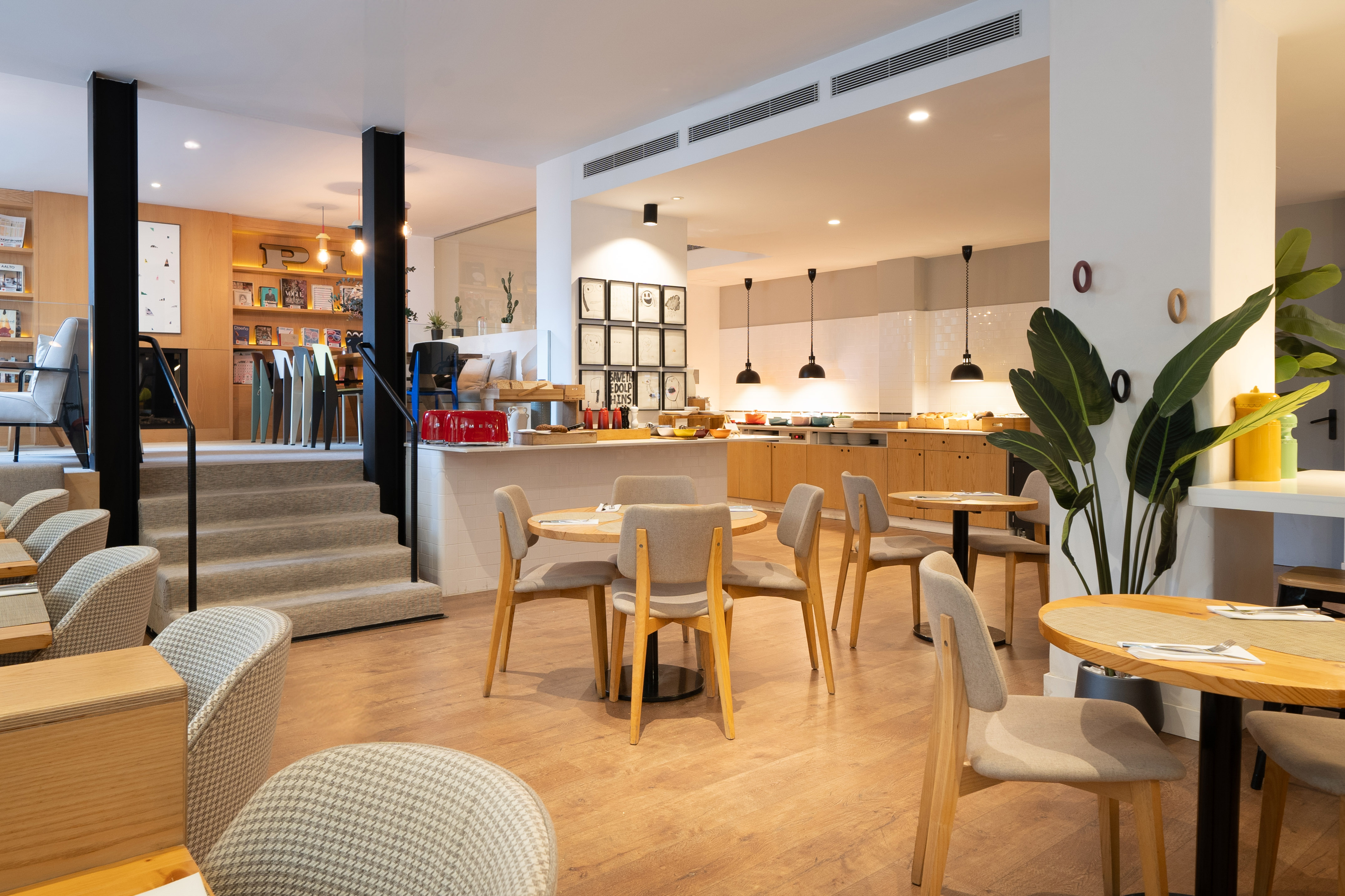 Modern hotel breakfast buffet and cafe with varied seating, lounge, and stairs.