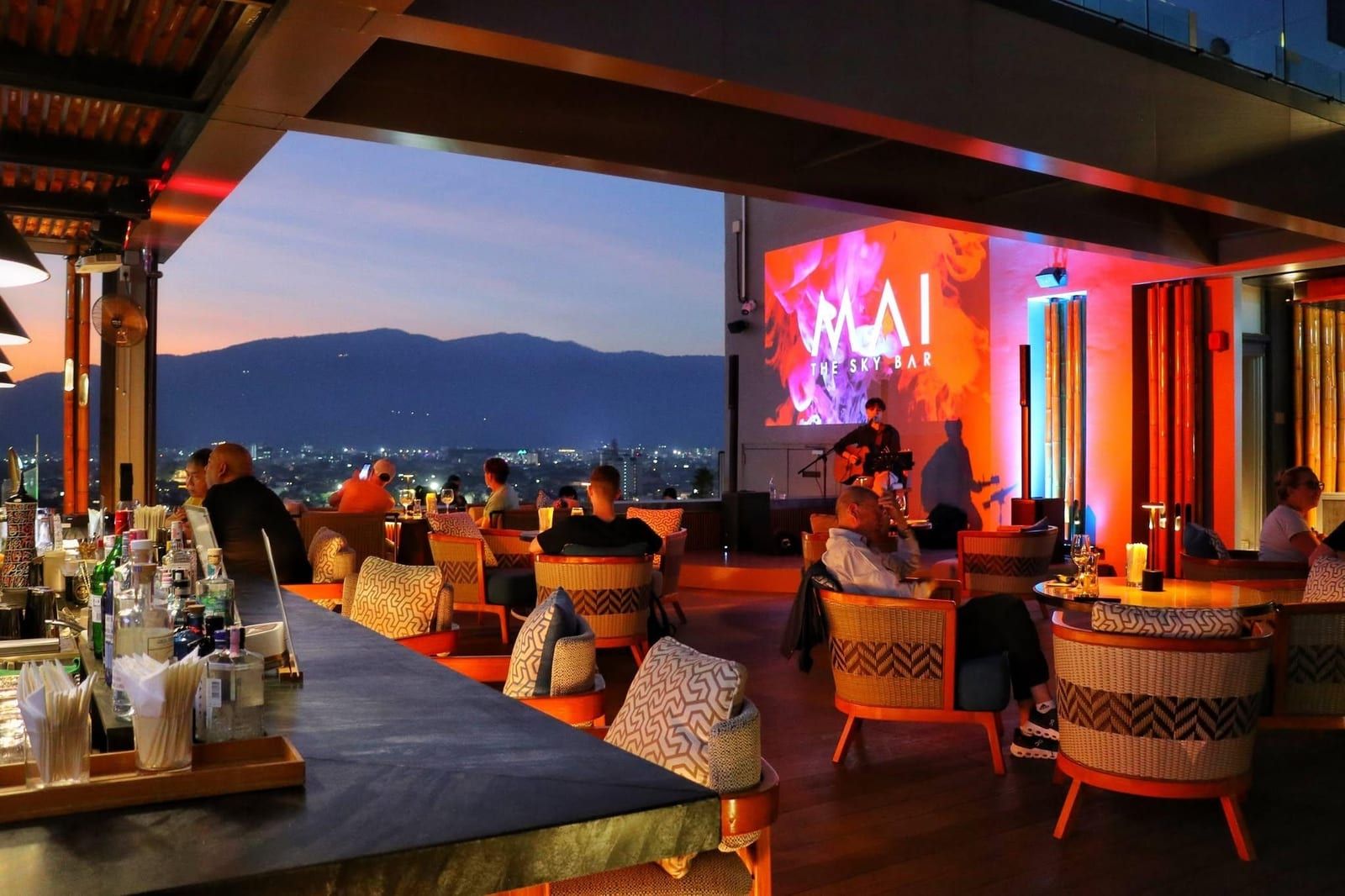 Mai Sky Bar at sunset with live music, mountain view, and patrons enjoying drinks.