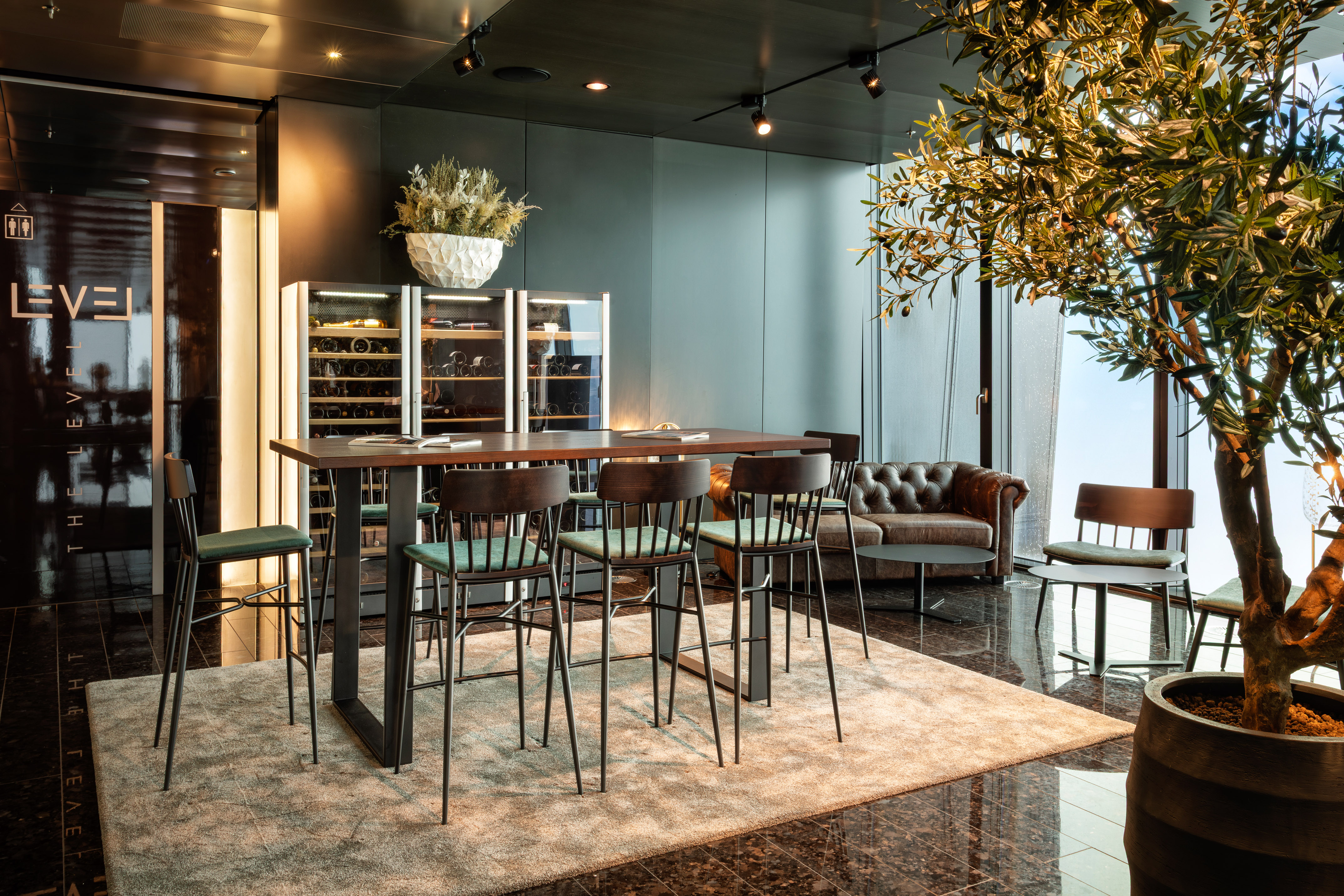 Hotel bar lounge with modern seating, wine fridges, and an olive tree.