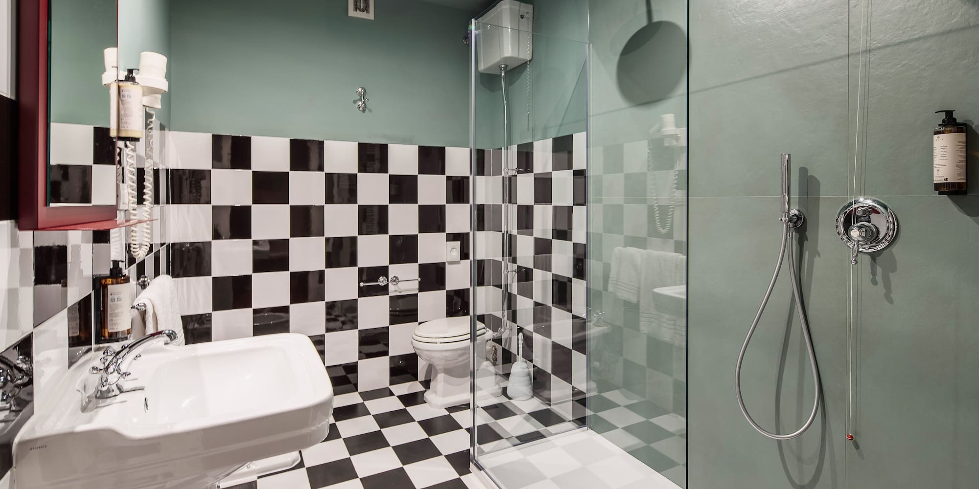 Modern bathroom with black & white checkered tiles, green walls, and glass shower.