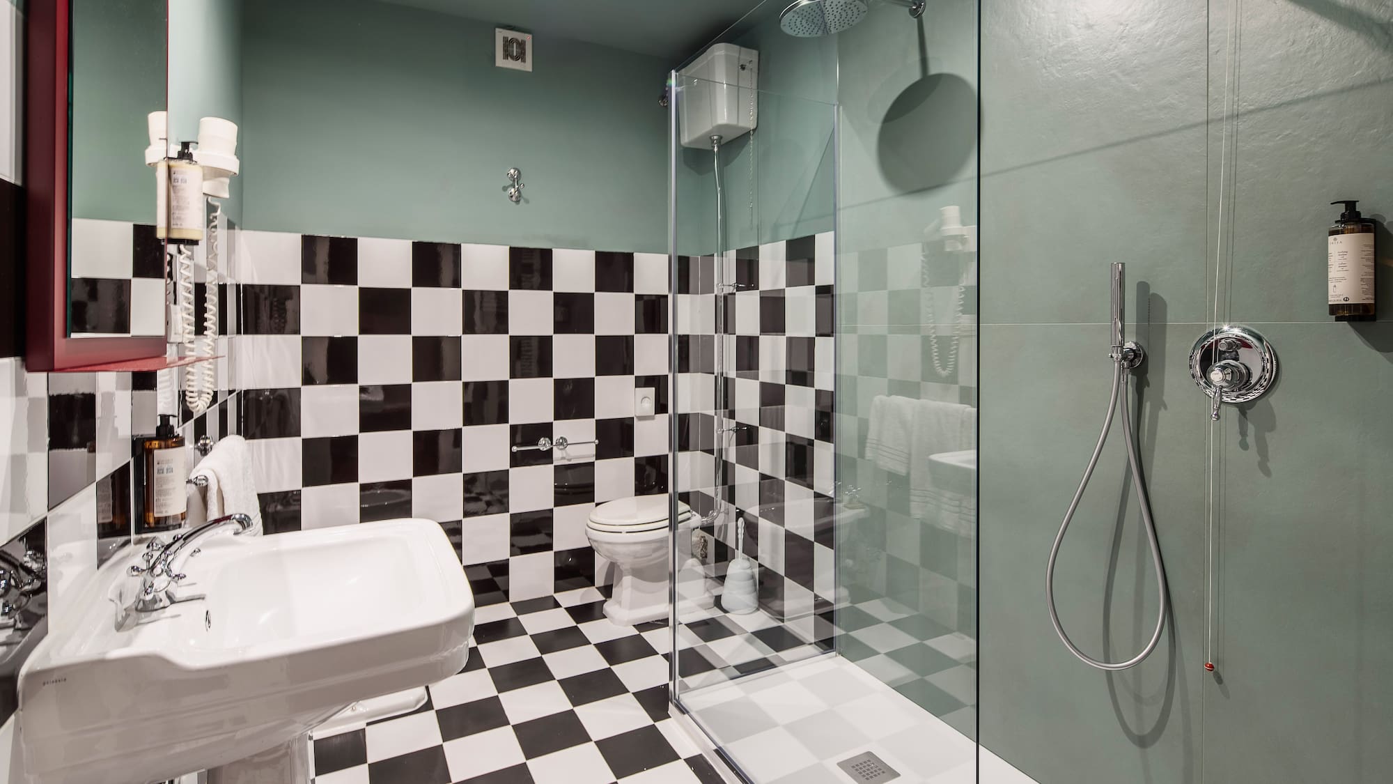 Green and checkerboard tiled bathroom with shower, sink, and toilet.