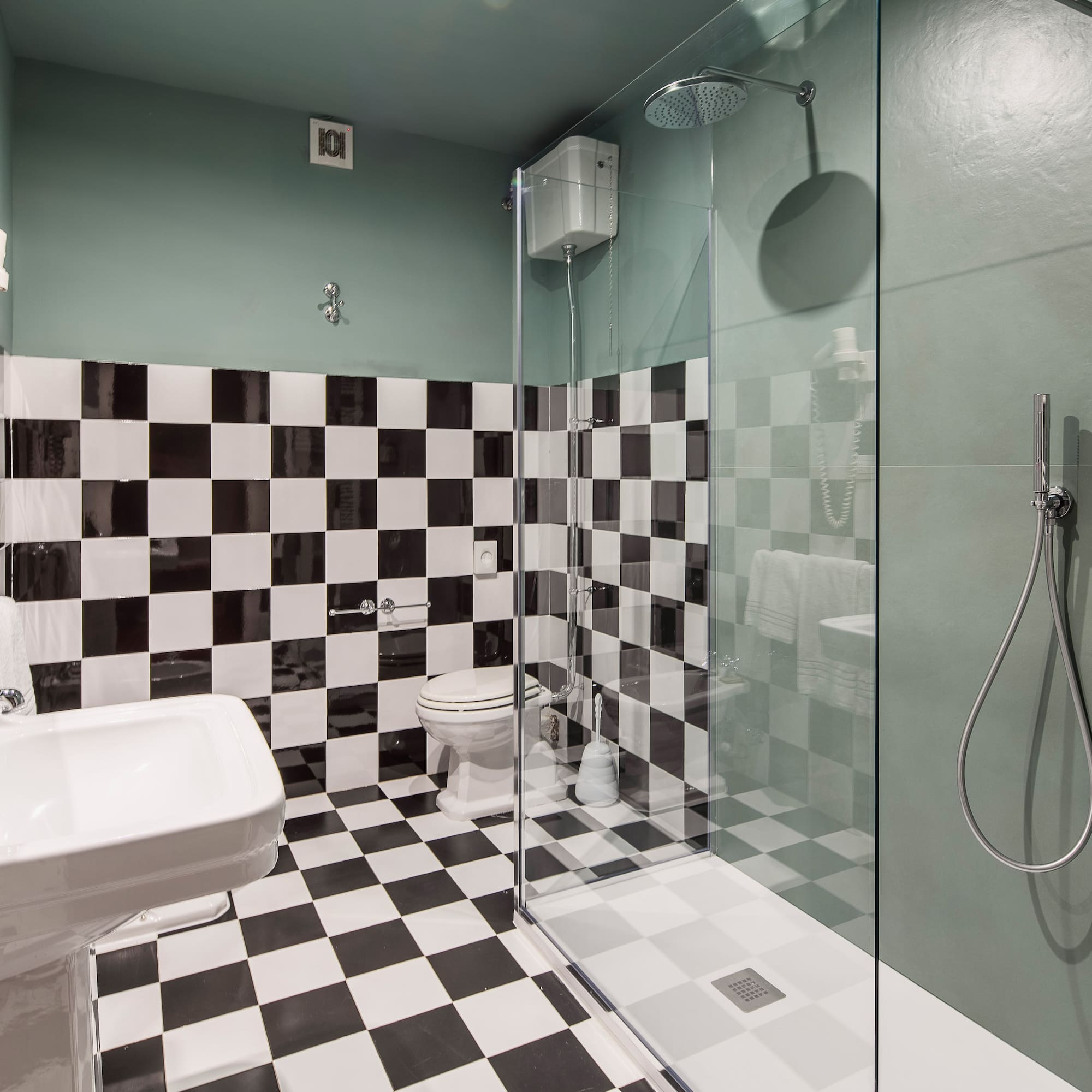 Modern bathroom with black & white checkered tiles, green walls, and glass shower.