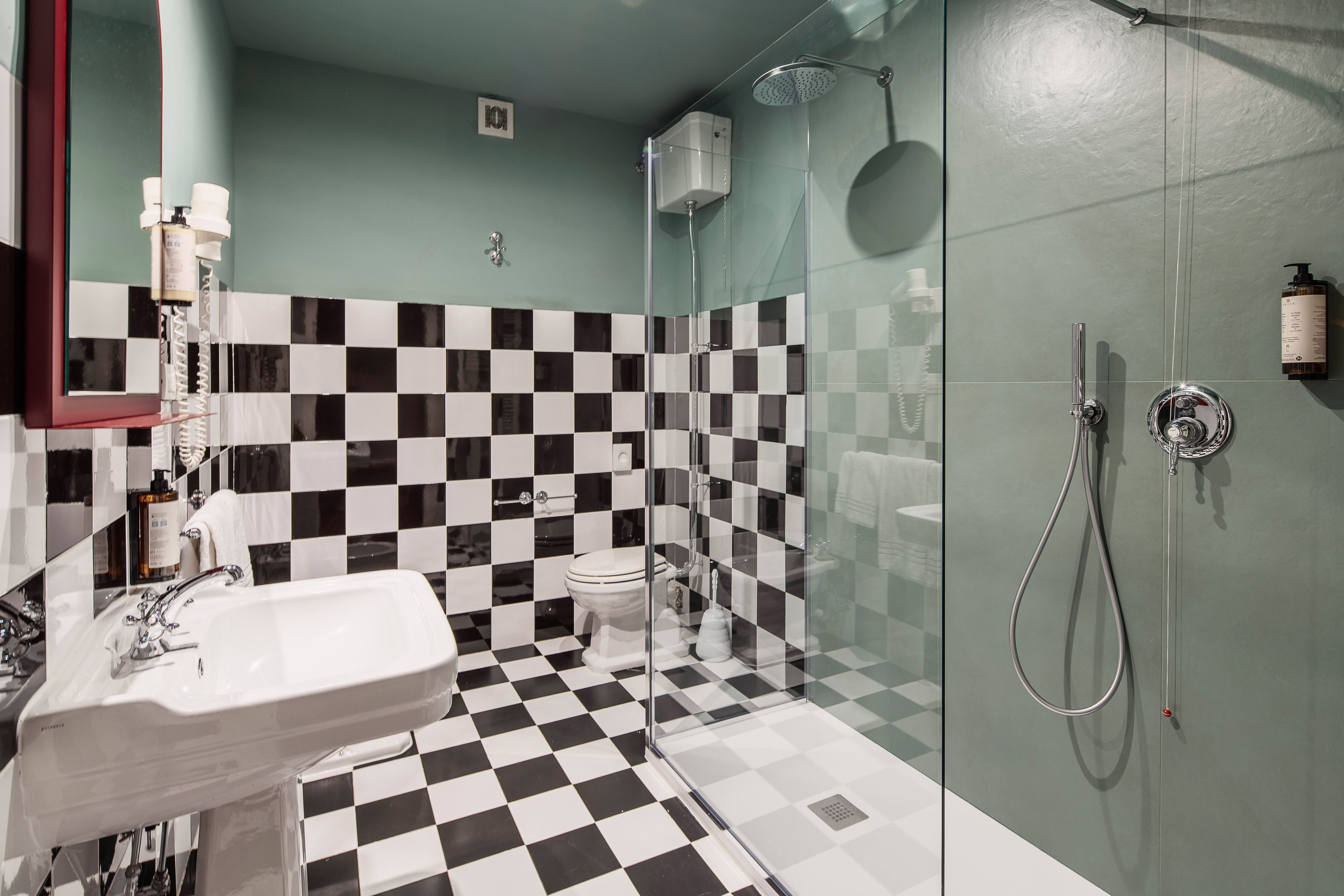 Modern bathroom with black & white checkered tiles, green walls, and glass shower.