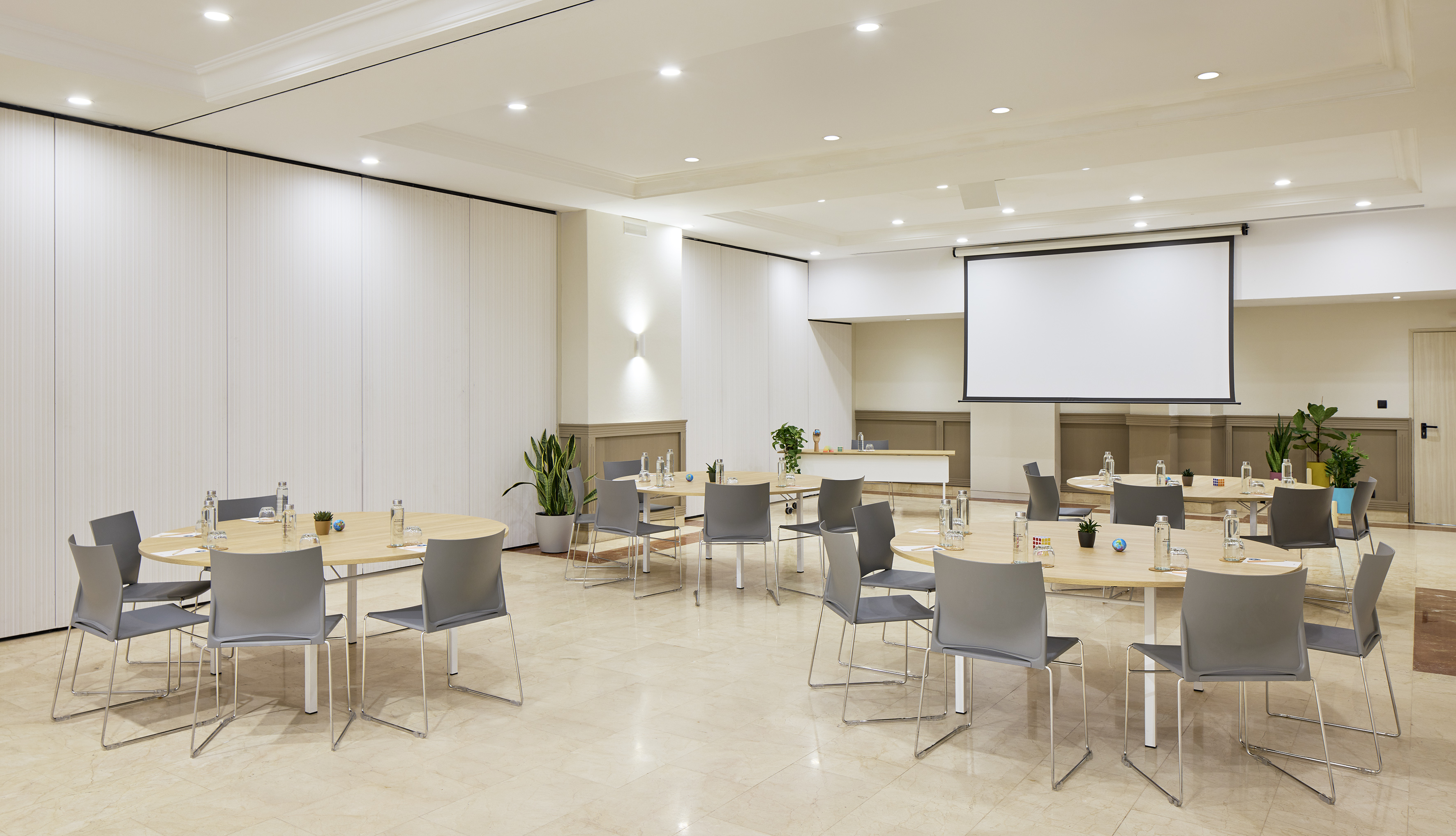 Modern conference room with round tables, gray chairs, and projector screen.