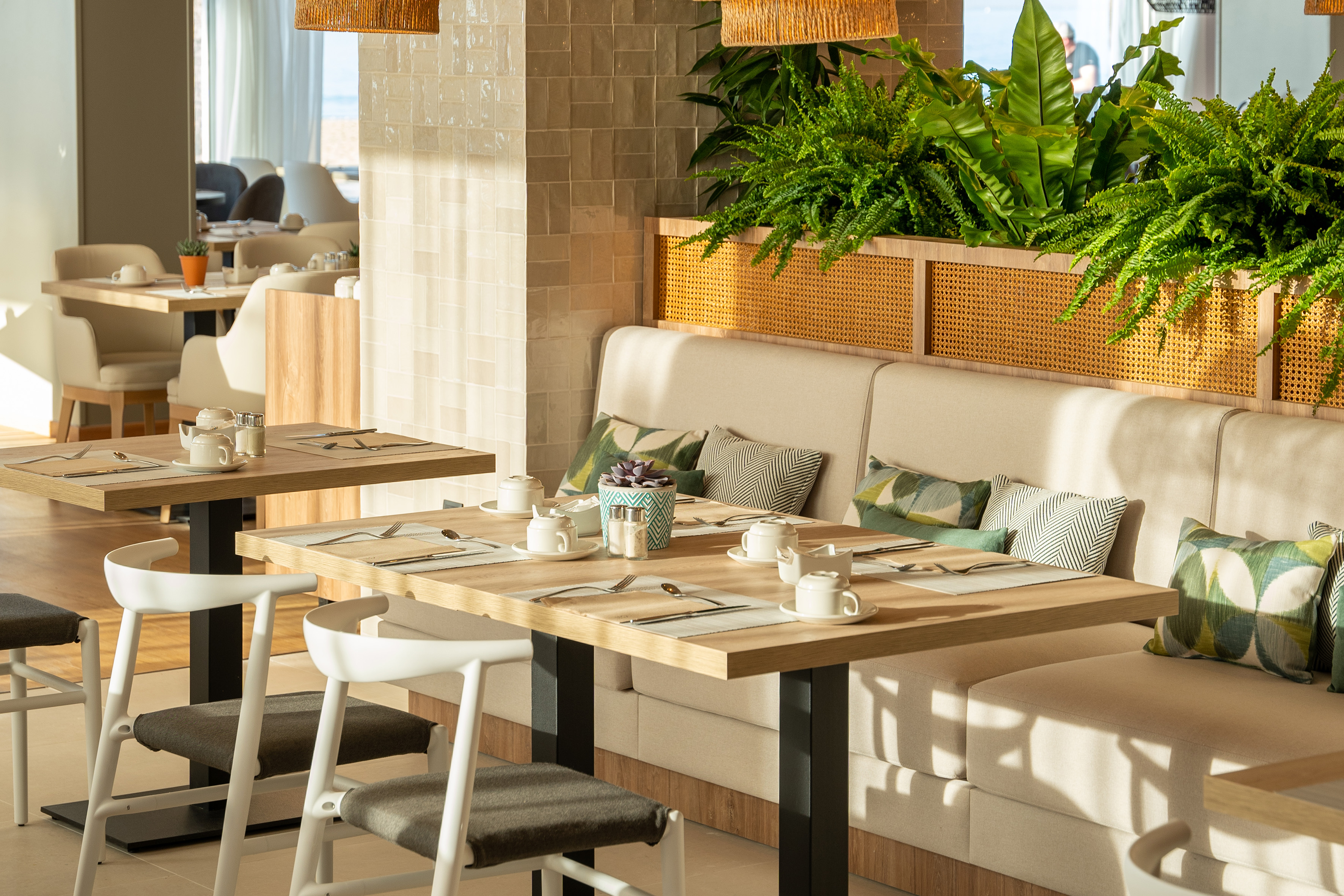 Contemporary hotel restaurant interior with set tables, banquettes, and ferns.