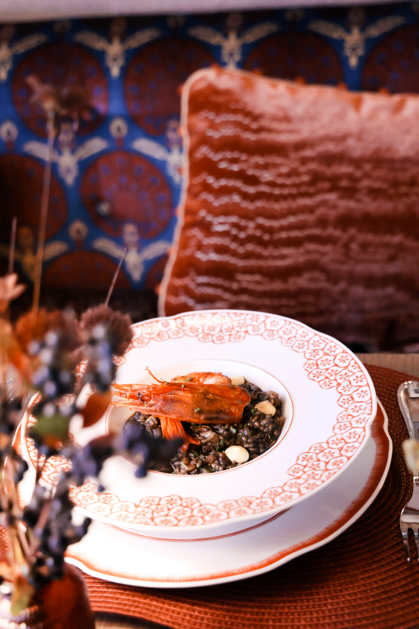 Squid ink rice with red shrimp in a decorative bowl on a dining table.