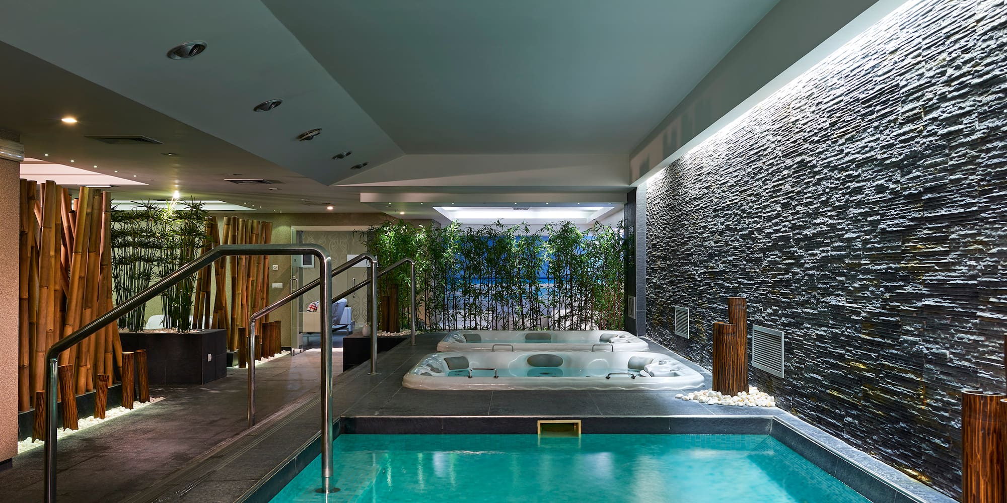 Indoor spa area with plunge pool, two jacuzzis, stone wall, and bamboo accents.