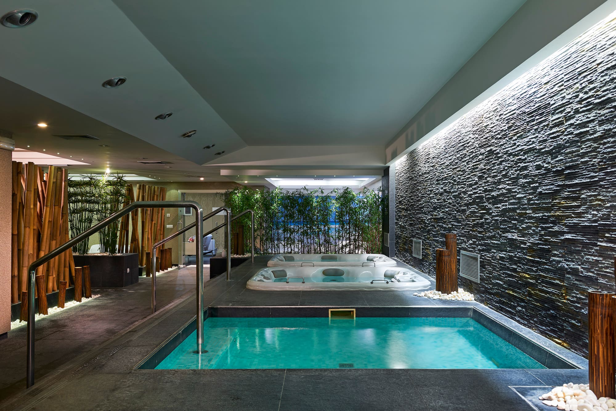 Indoor spa area with plunge pool, two jacuzzis, stone wall, and bamboo accents.