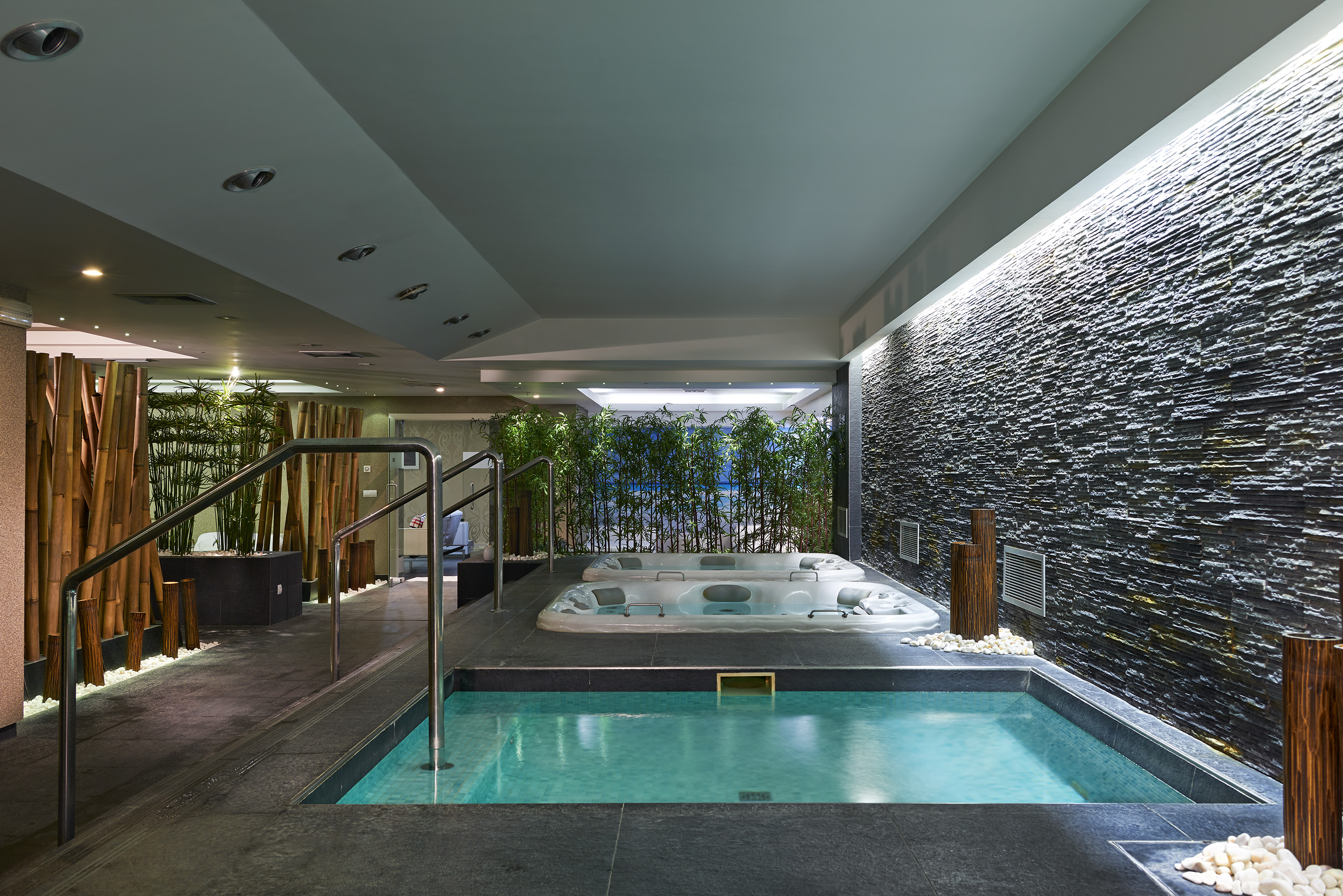 Indoor spa area with plunge pool, two jacuzzis, stone wall, and bamboo accents.
