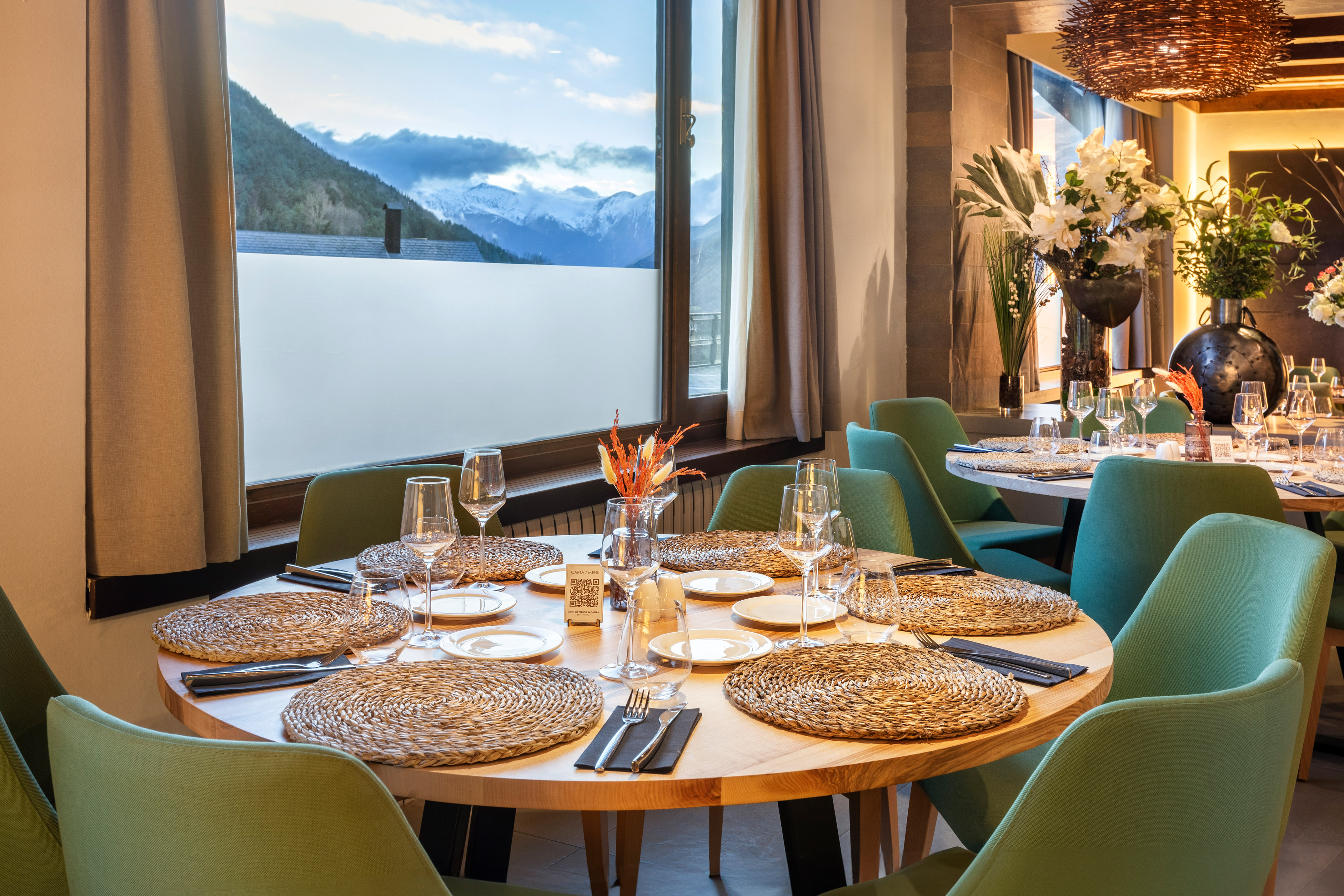 Mesa de restaurante con sillas verdes y vistas a montañas nevadas.