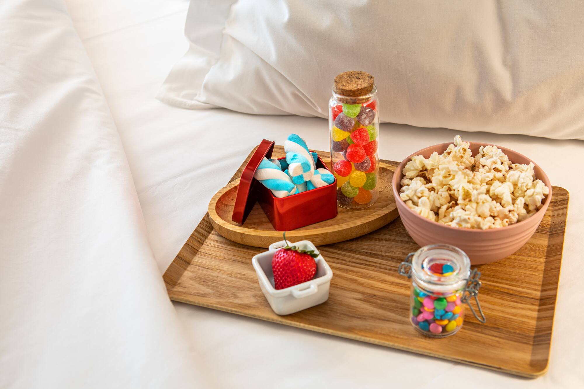 Snacks on bed tray: popcorn, marshmallows, jelly candies, chocolates, strawberry.