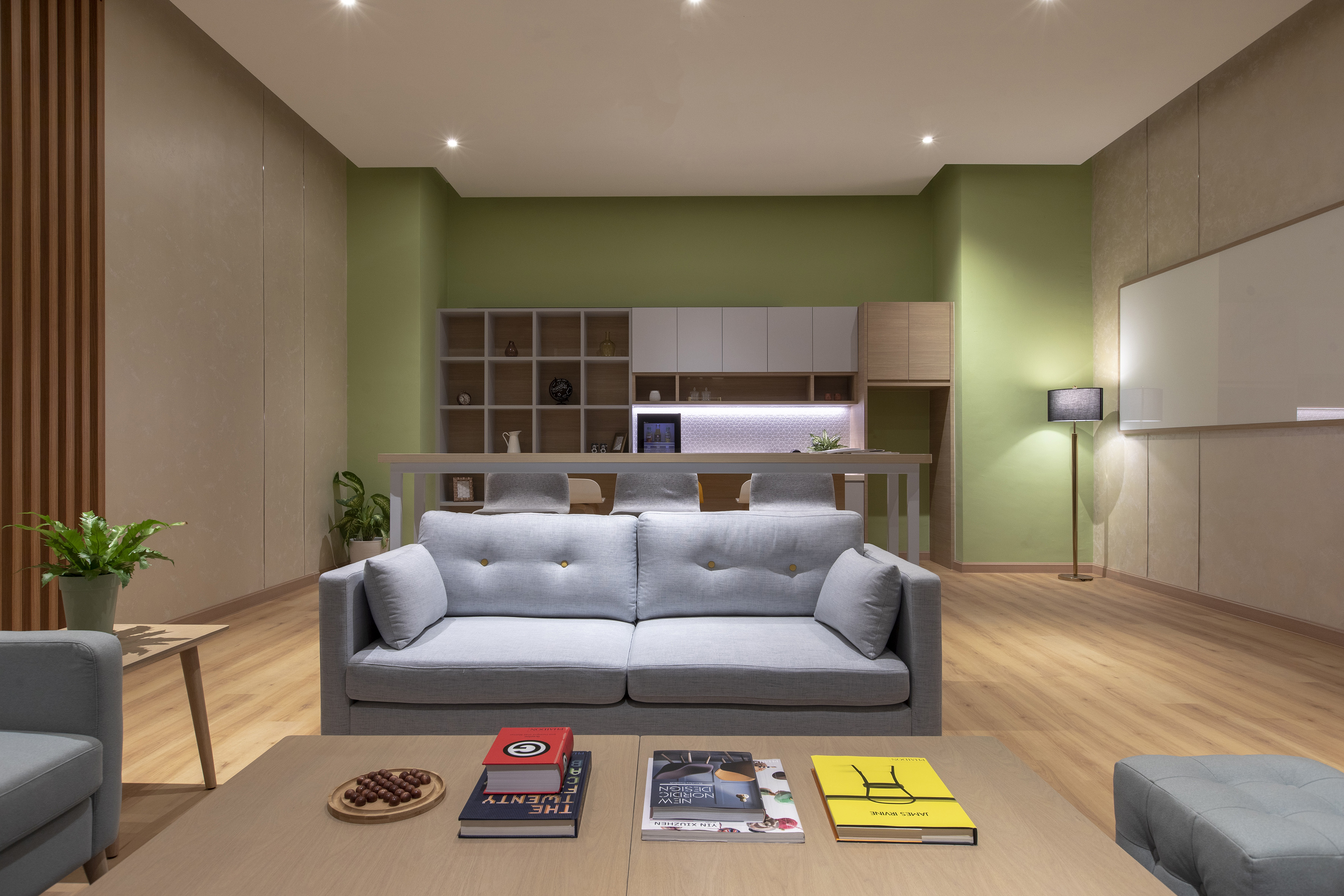 Modern gray sofa in contemporary living room with green accent wall and kitchenette.
