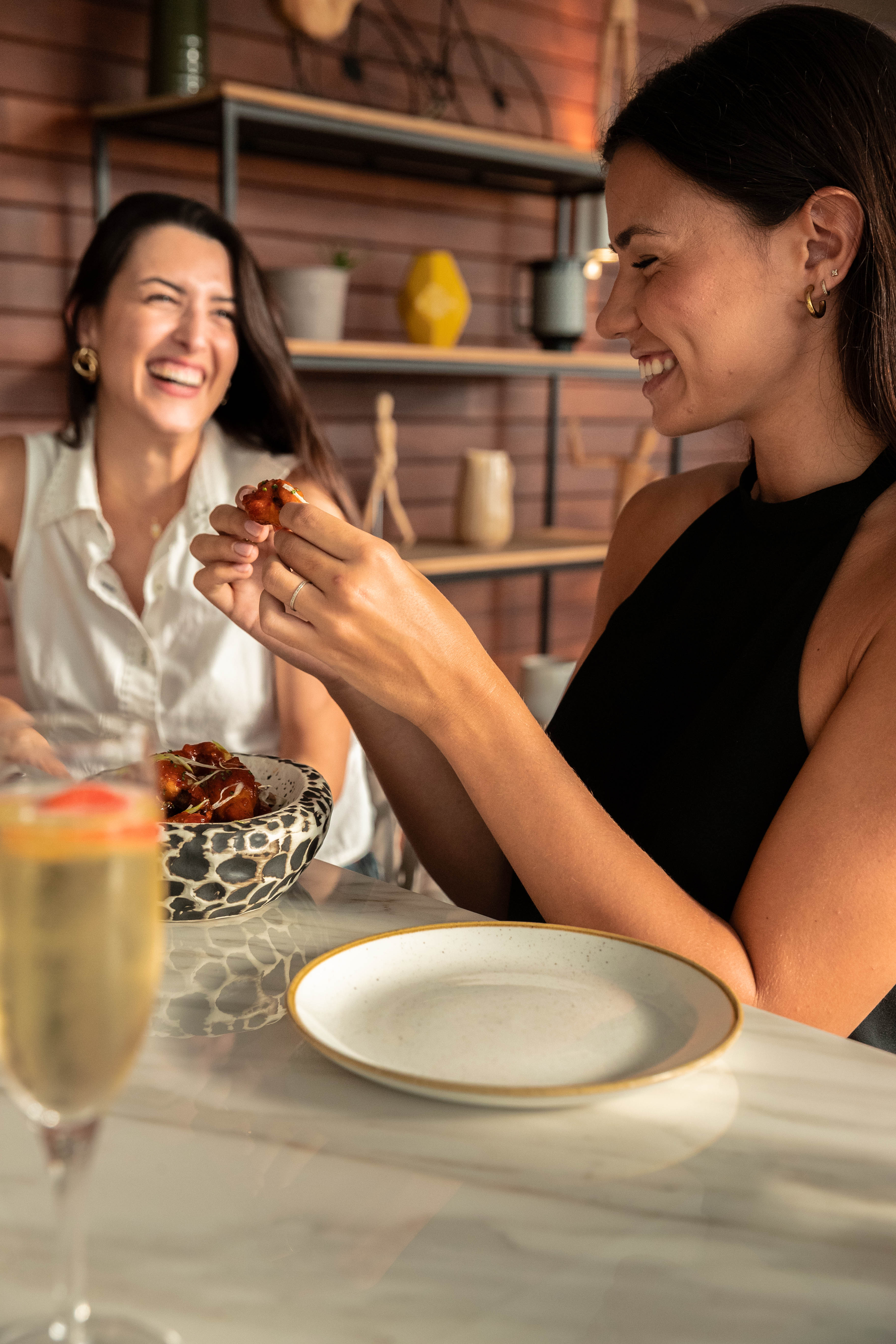 Two women laughing and eating appetizers at a restaurant table.