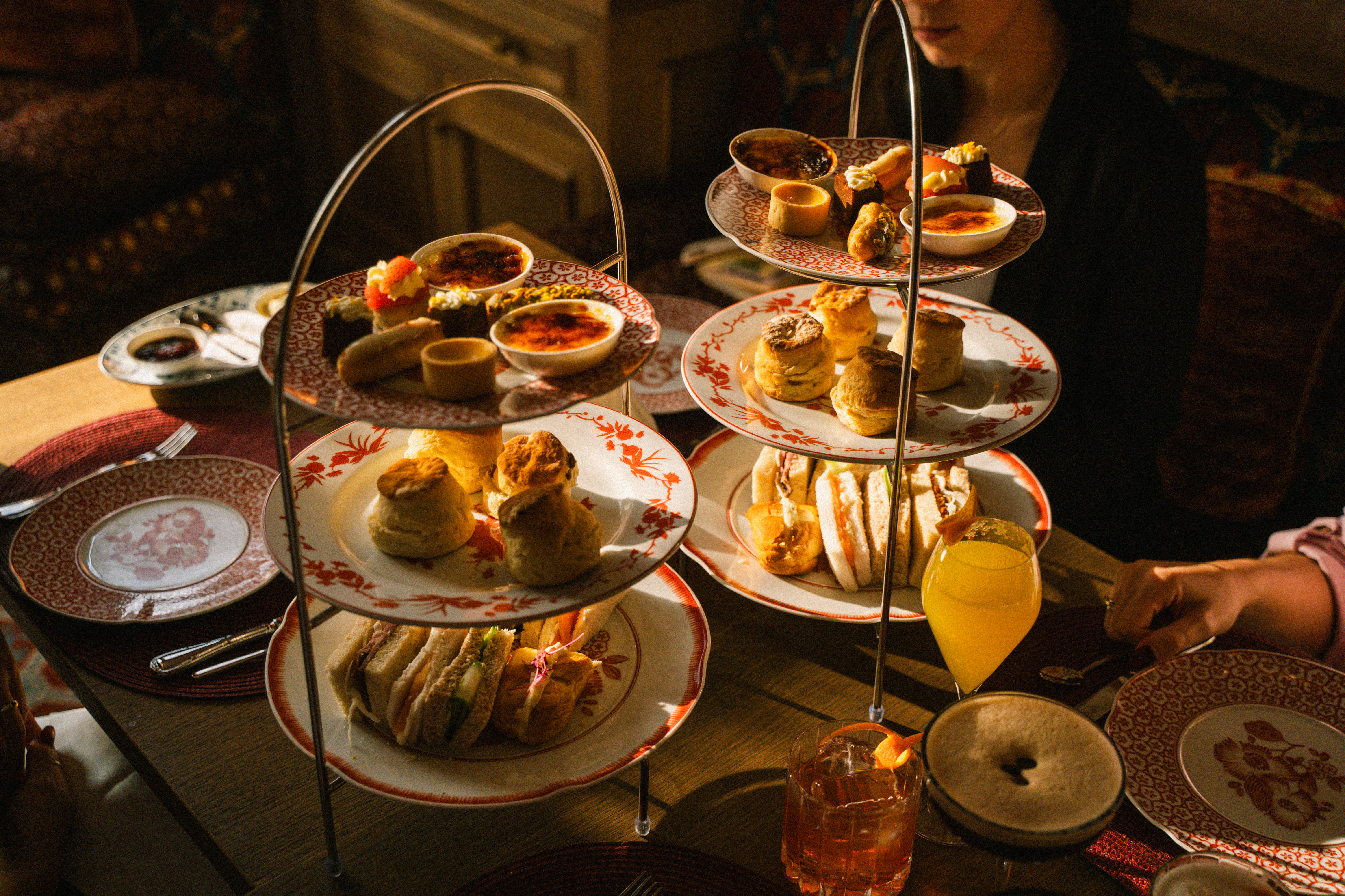 Warm light on tiered stands of afternoon tea: scones, sandwiches, mini desserts.