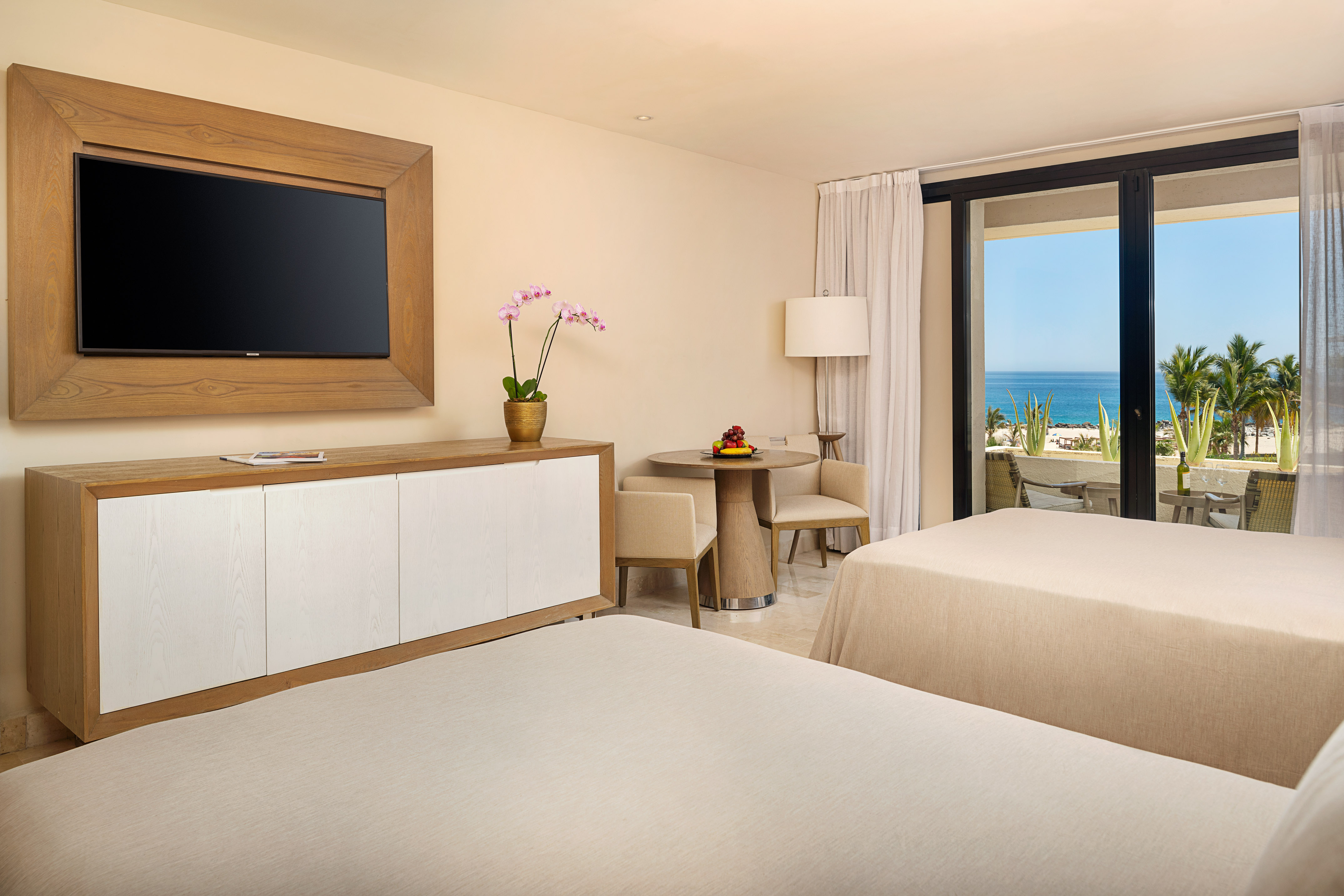 Luxury resort room with two beds, ocean view balcony, and TV.