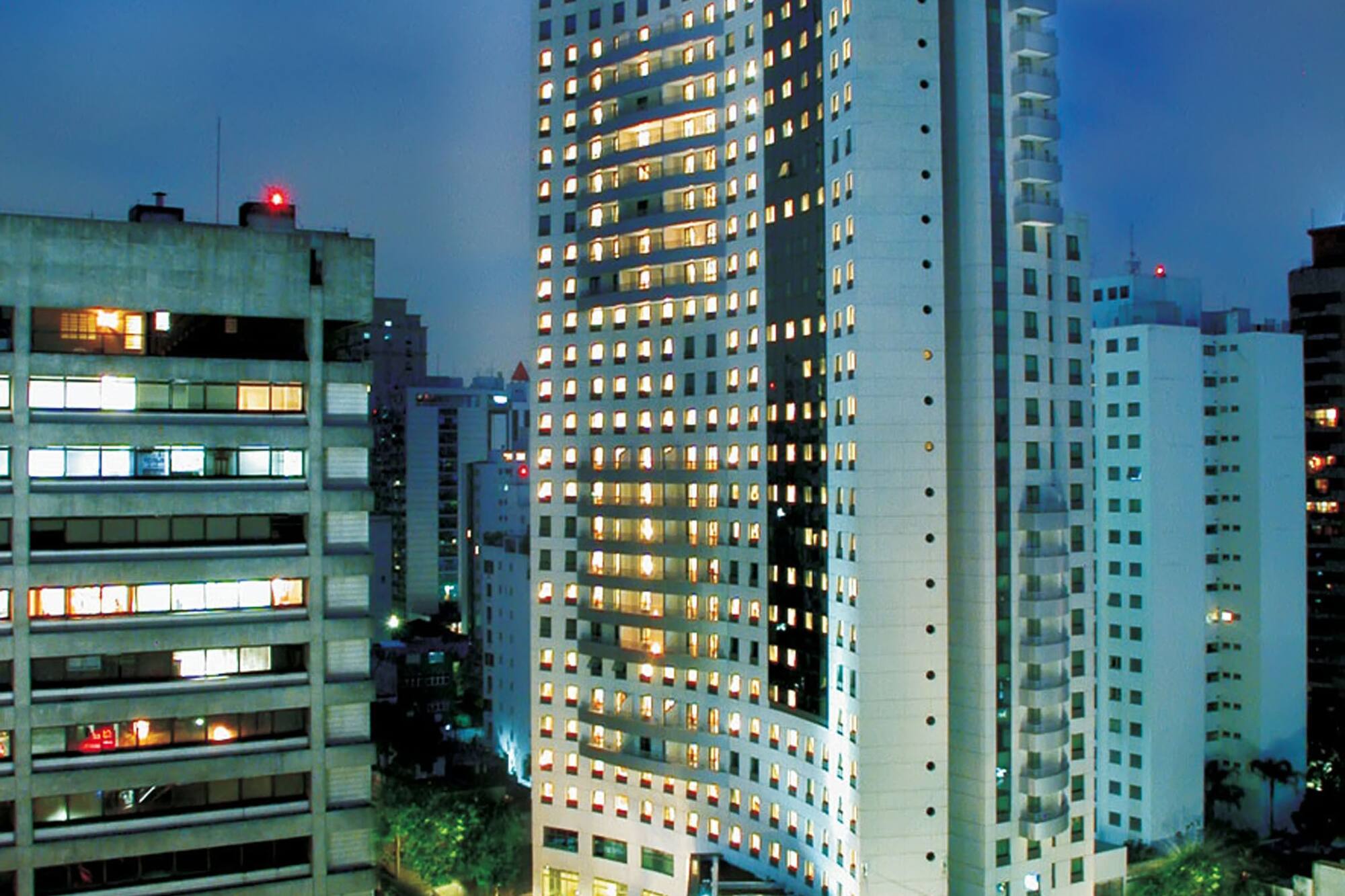 Tall, curved modern building with illuminated windows in a city at dusk.