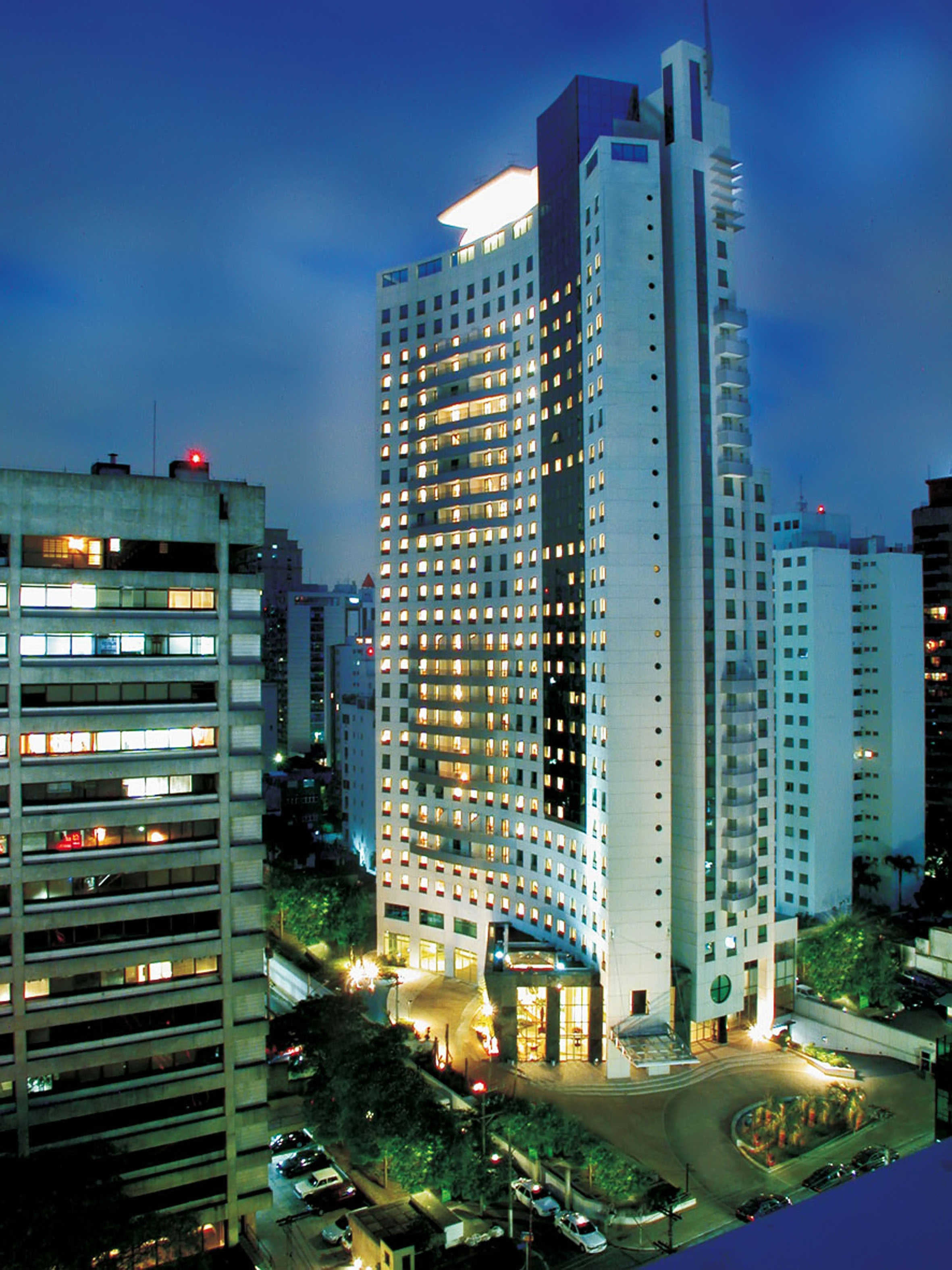 Tall, curved modern building with illuminated windows in a city at dusk.