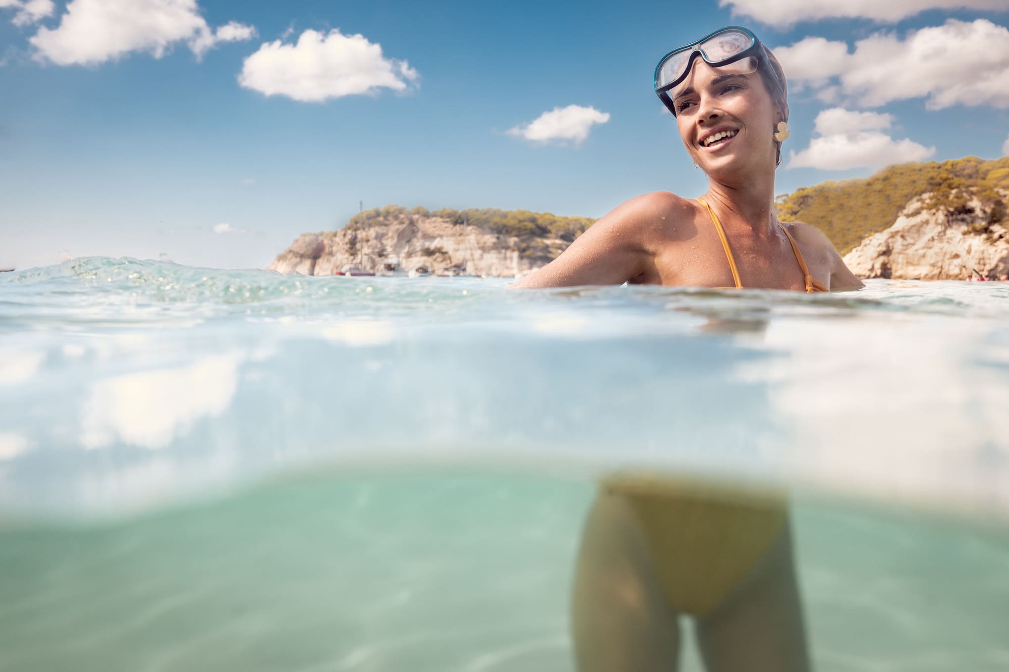 Mujer sonriente con gafas de buceo en el mar, costa al fondo.