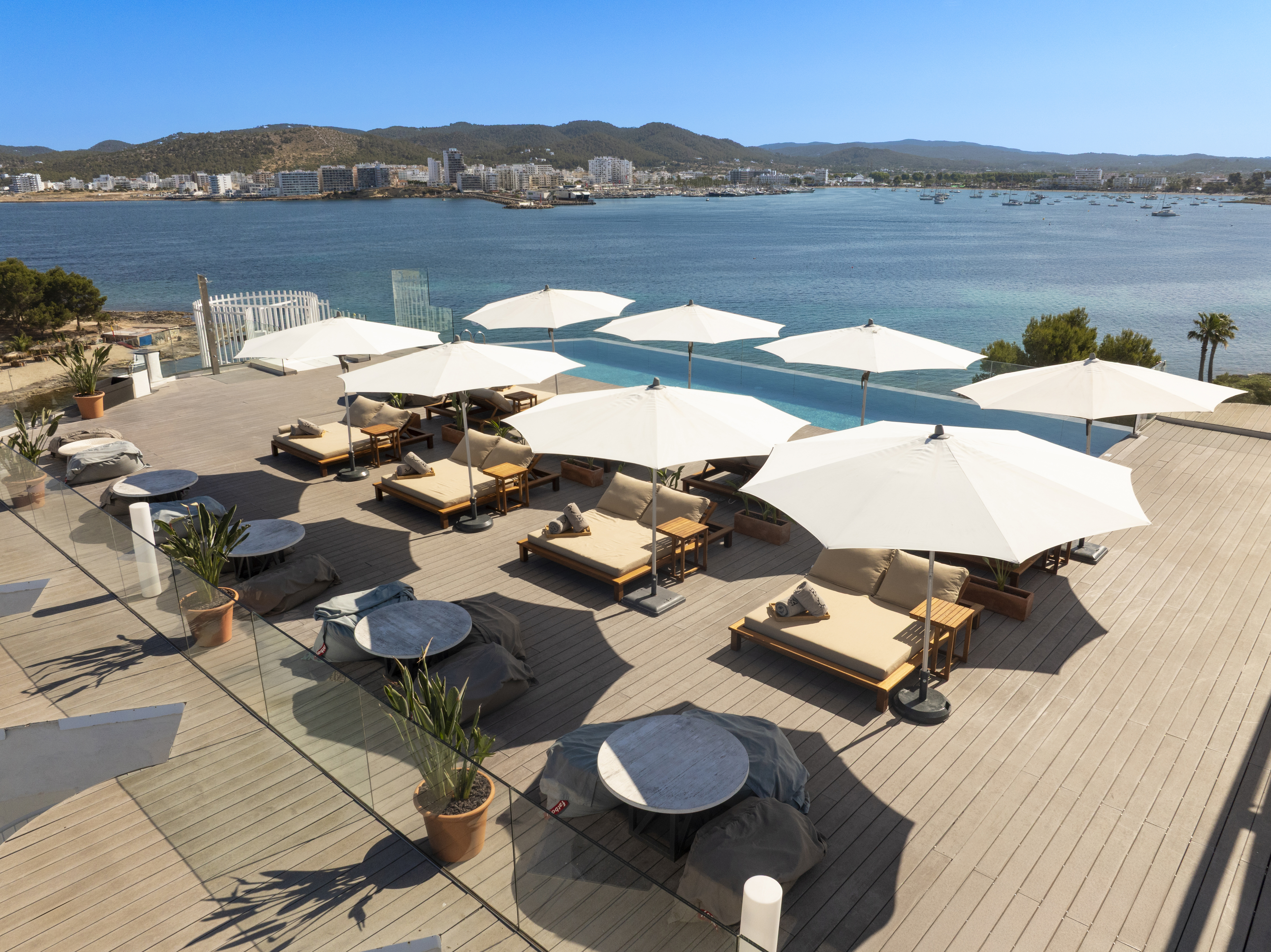 Rooftop infinity pool, sun loungers, umbrellas, and boats in a sunny bay.
