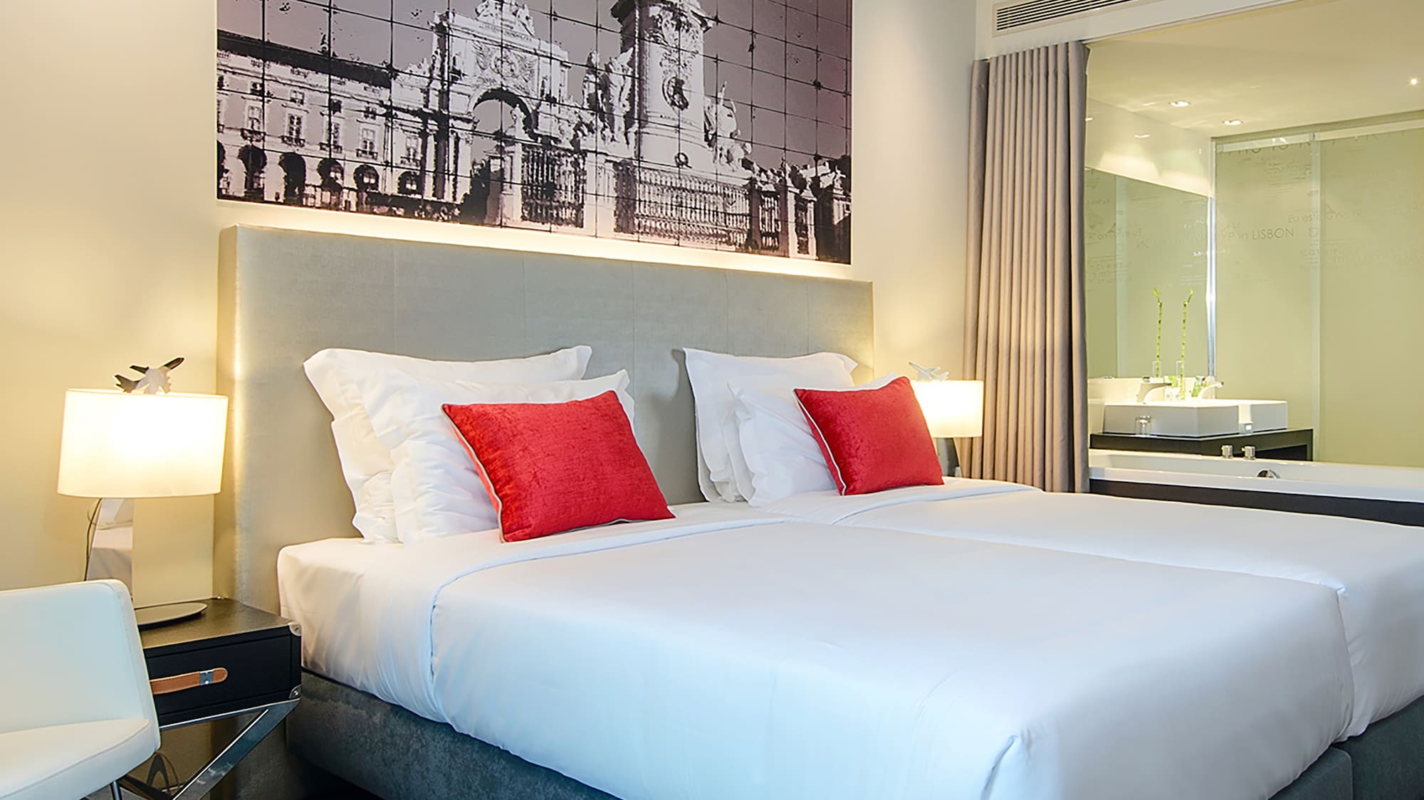 Modern hotel bedroom with twin beds, Lisbon city mural, and red pillows.
