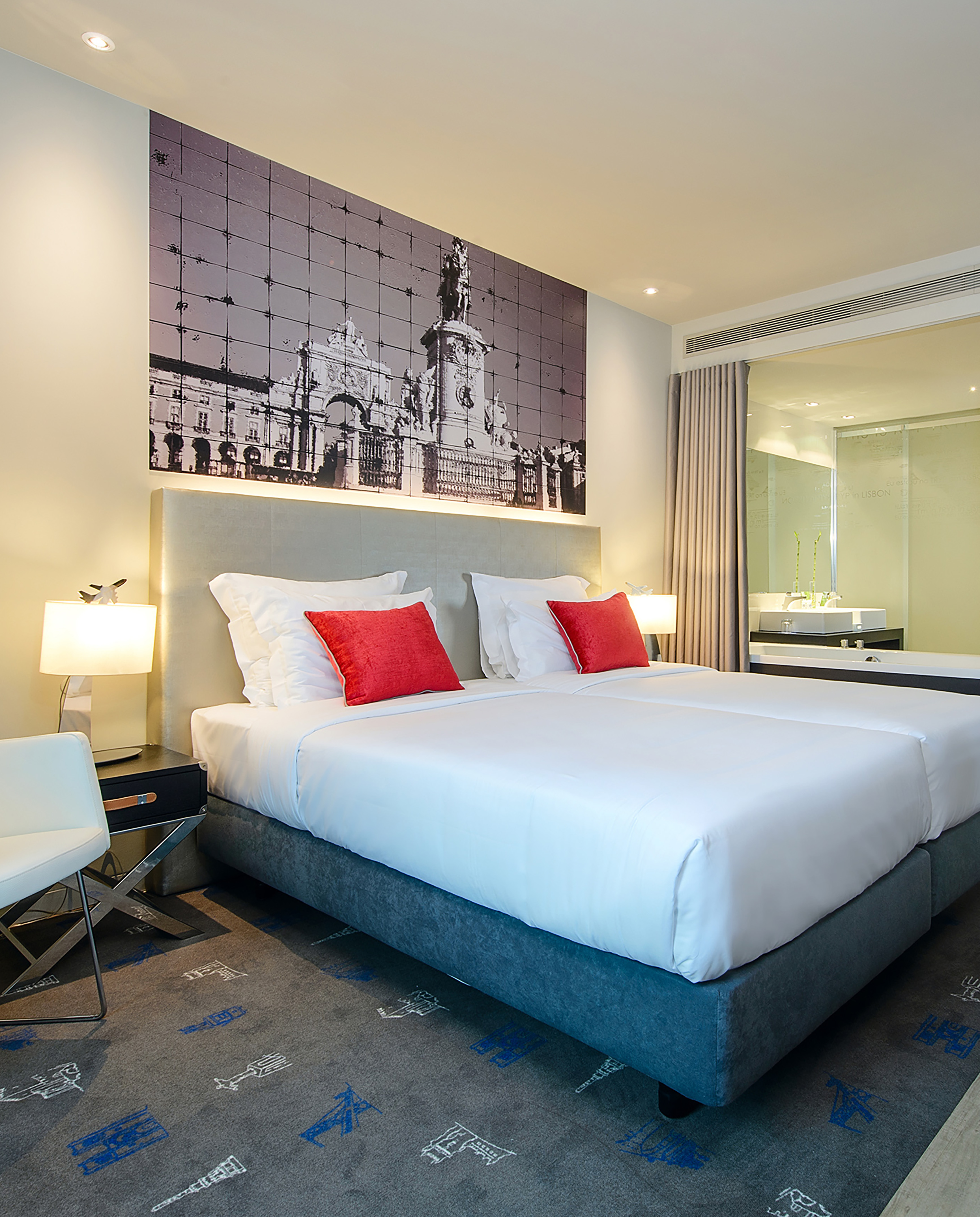 Modern hotel bedroom with twin beds, Lisbon city mural, and red pillows.