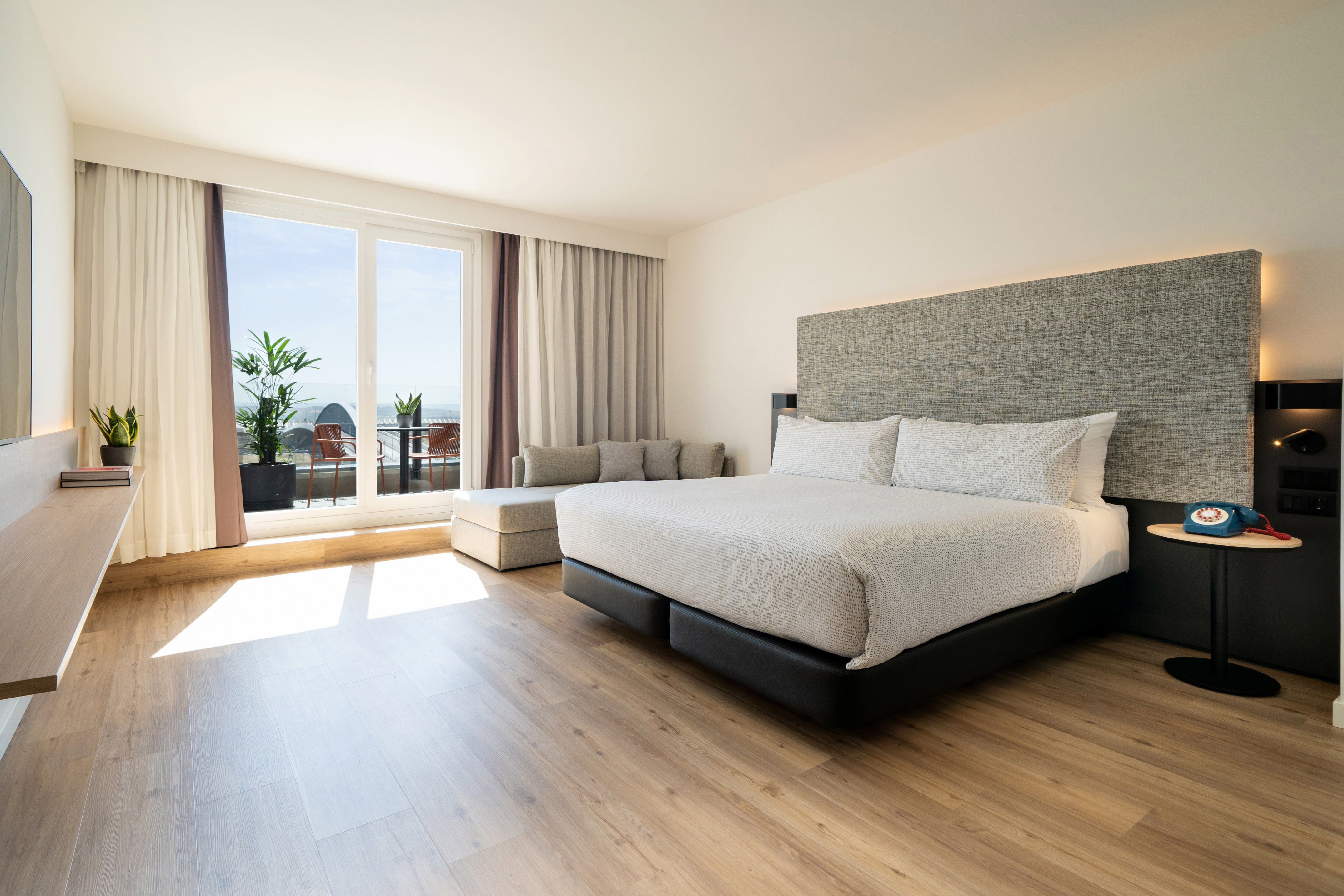 Modern hotel room with king bed, sofa, balcony, and ocean view.