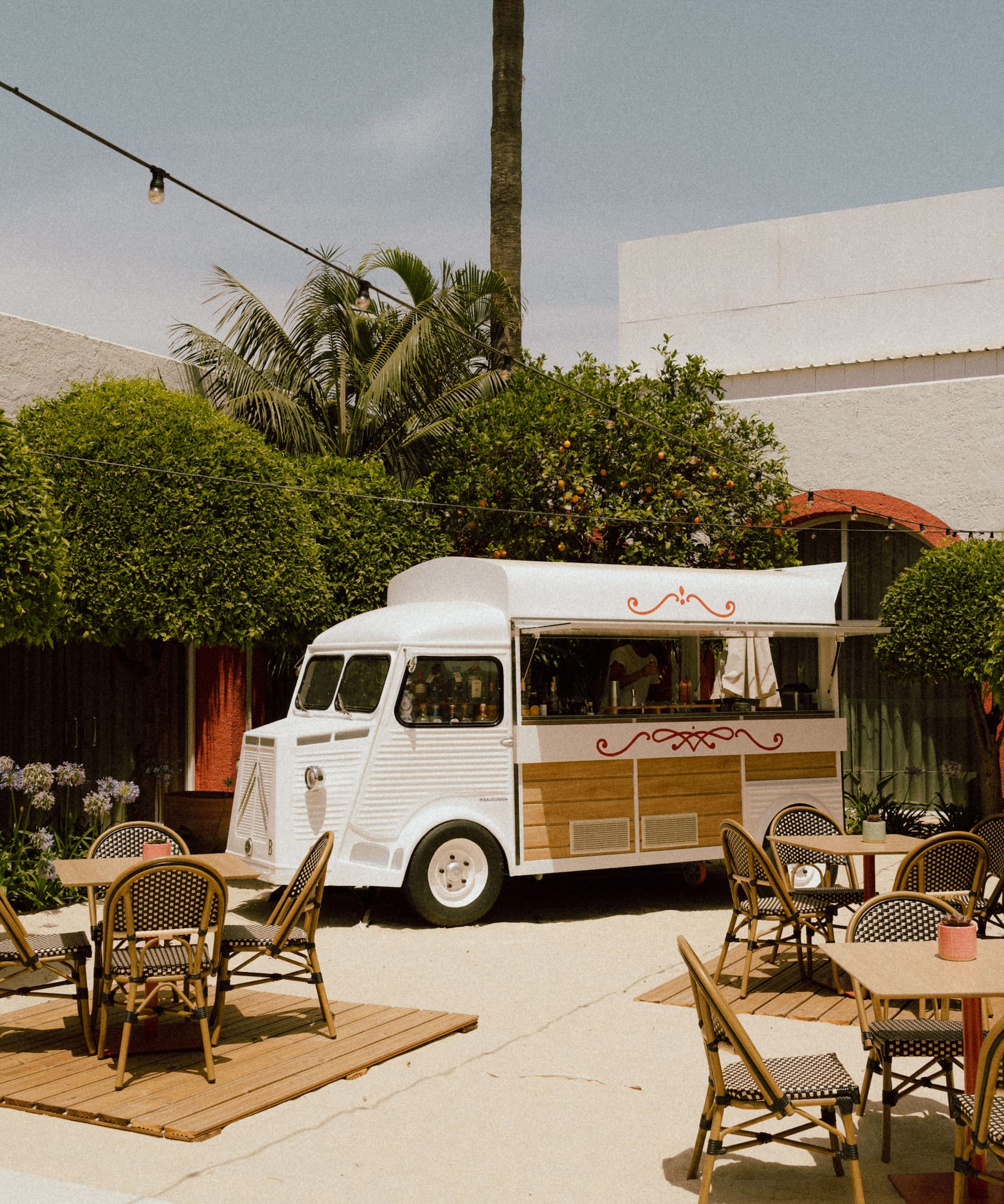 Vintage food truck on patio with bistro tables, palm trees & string lights.