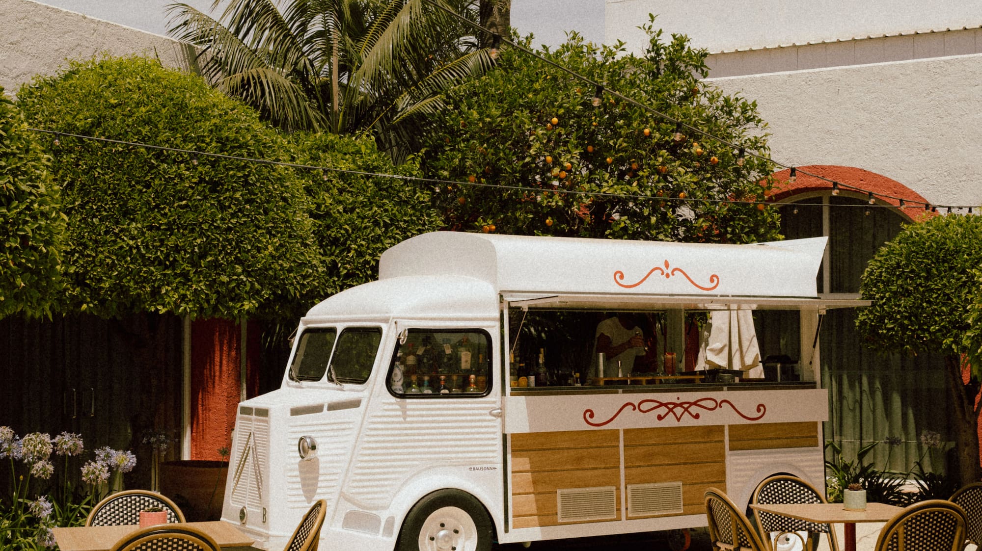 White vintage food truck bar in a sunny outdoor patio with bistro tables.