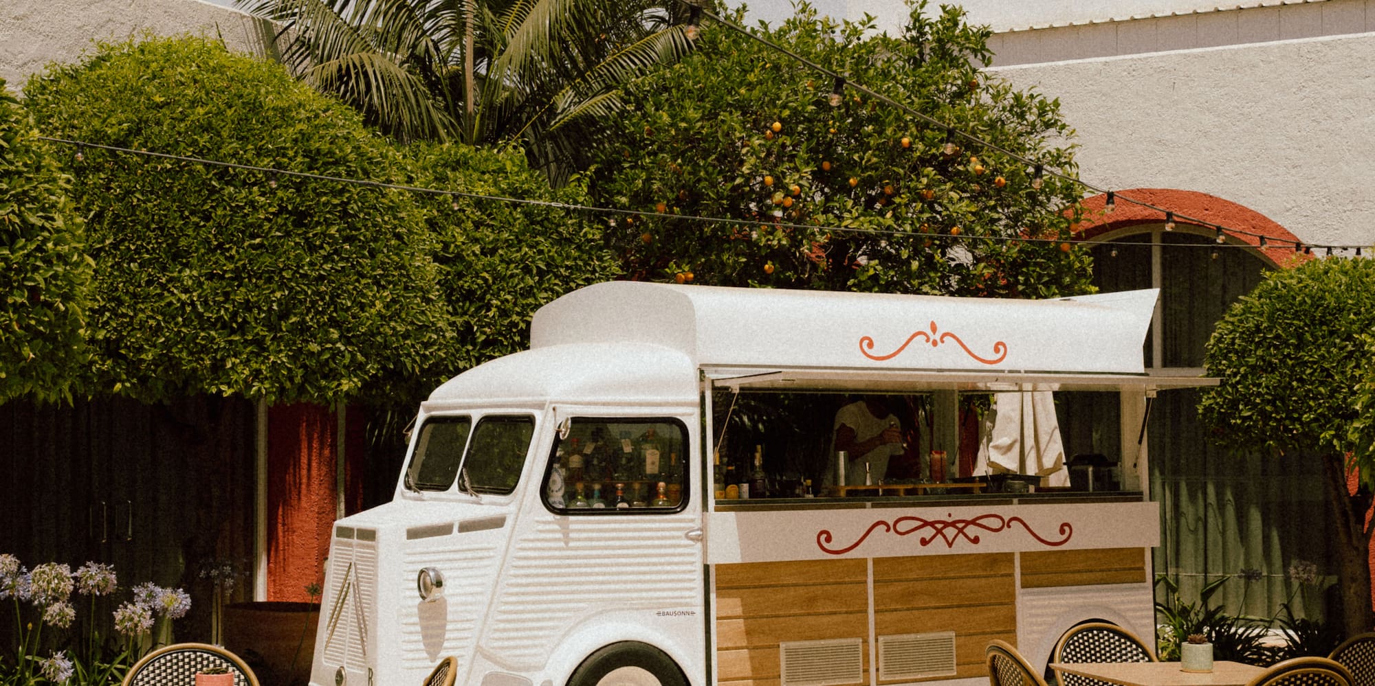 Vintage food truck on patio with bistro tables, palm trees & string lights.