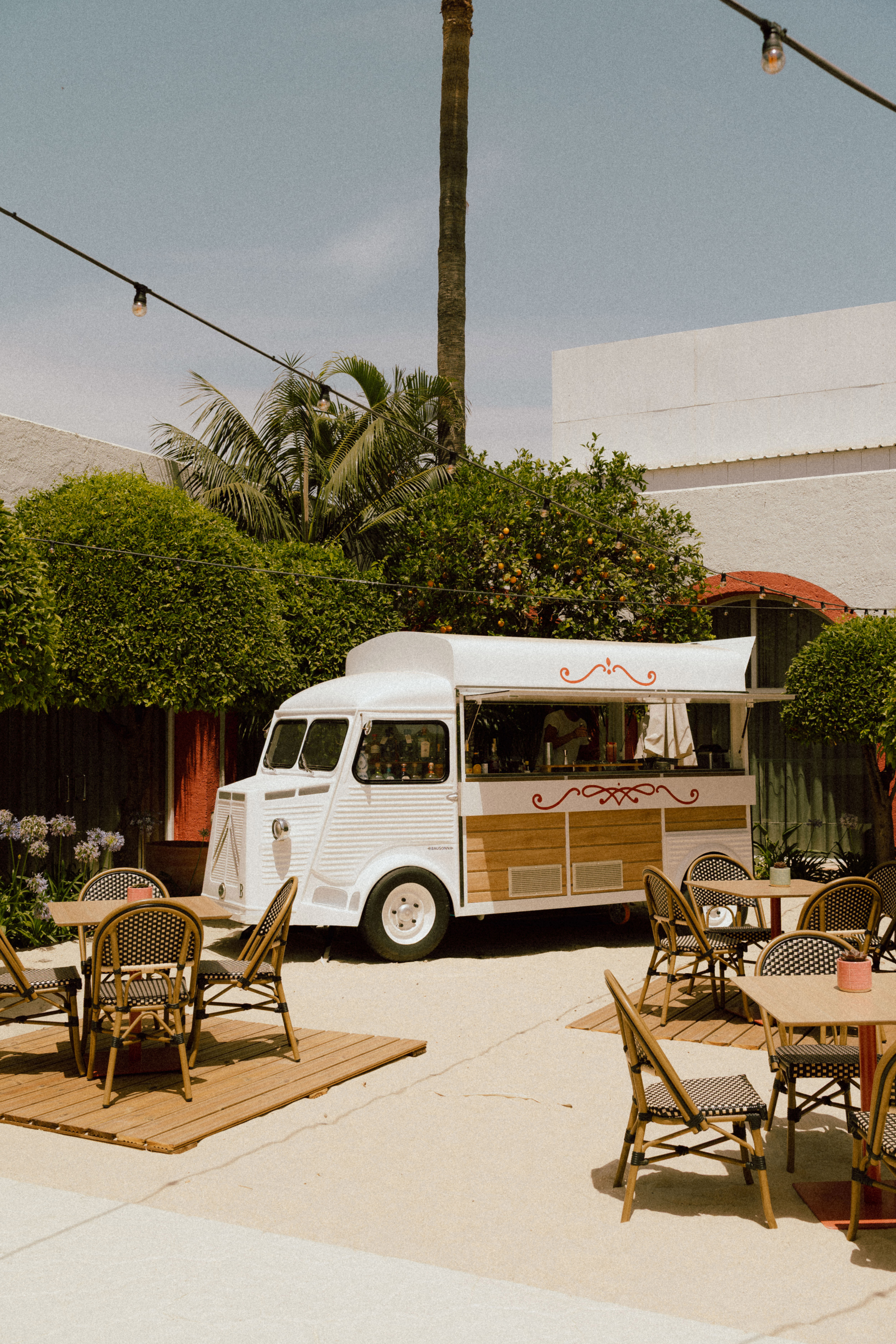 White vintage food truck bar in a sunny outdoor patio with bistro tables.